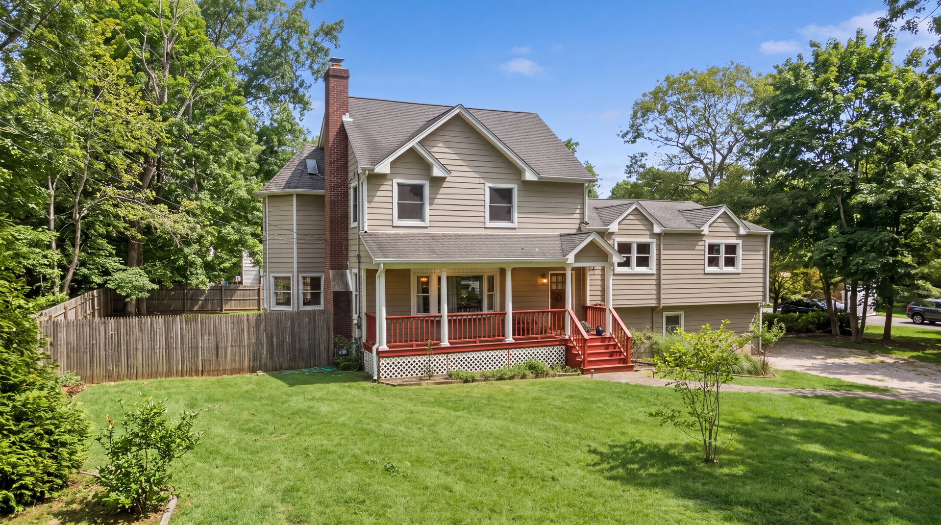 Two-story beige house with a red-railed porch, brick chimney, and broad green lawn.
