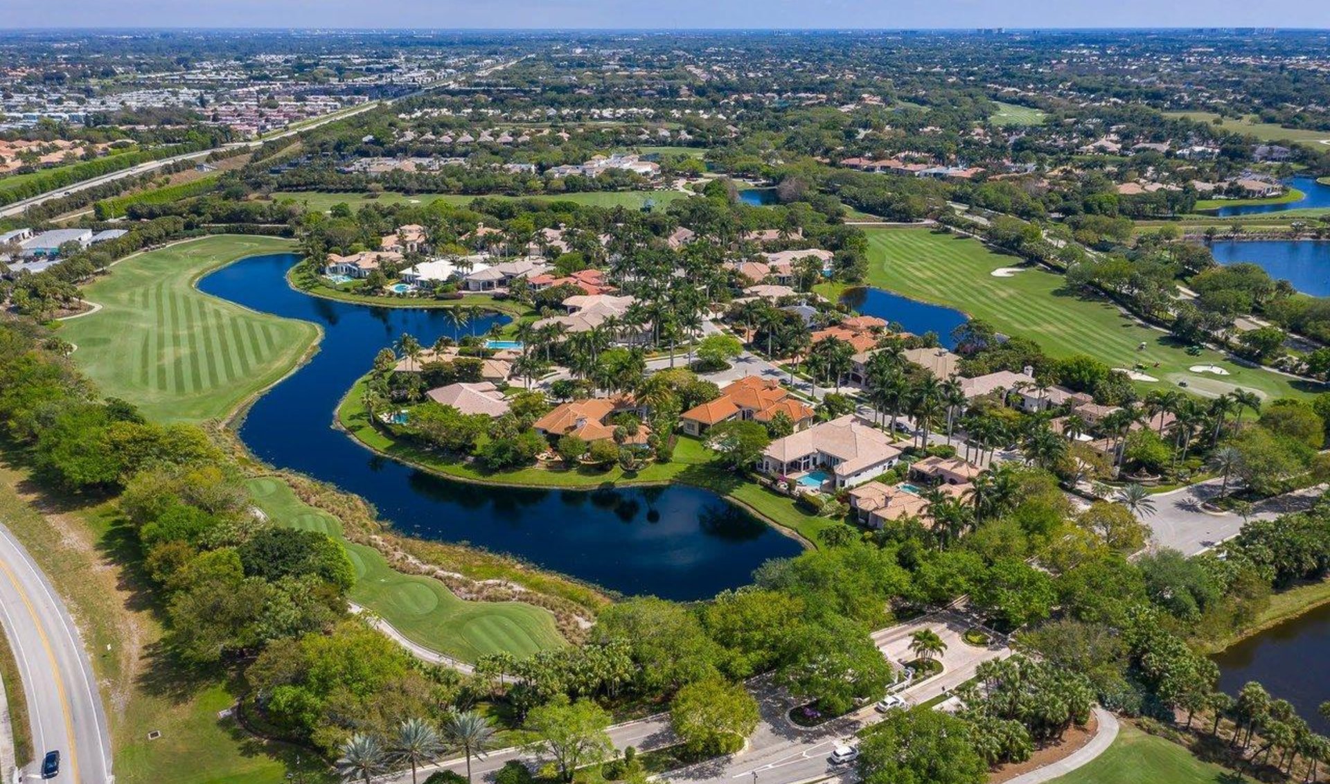 Aerial view of a golf community with homes beside winding lakes and manicured fairways.