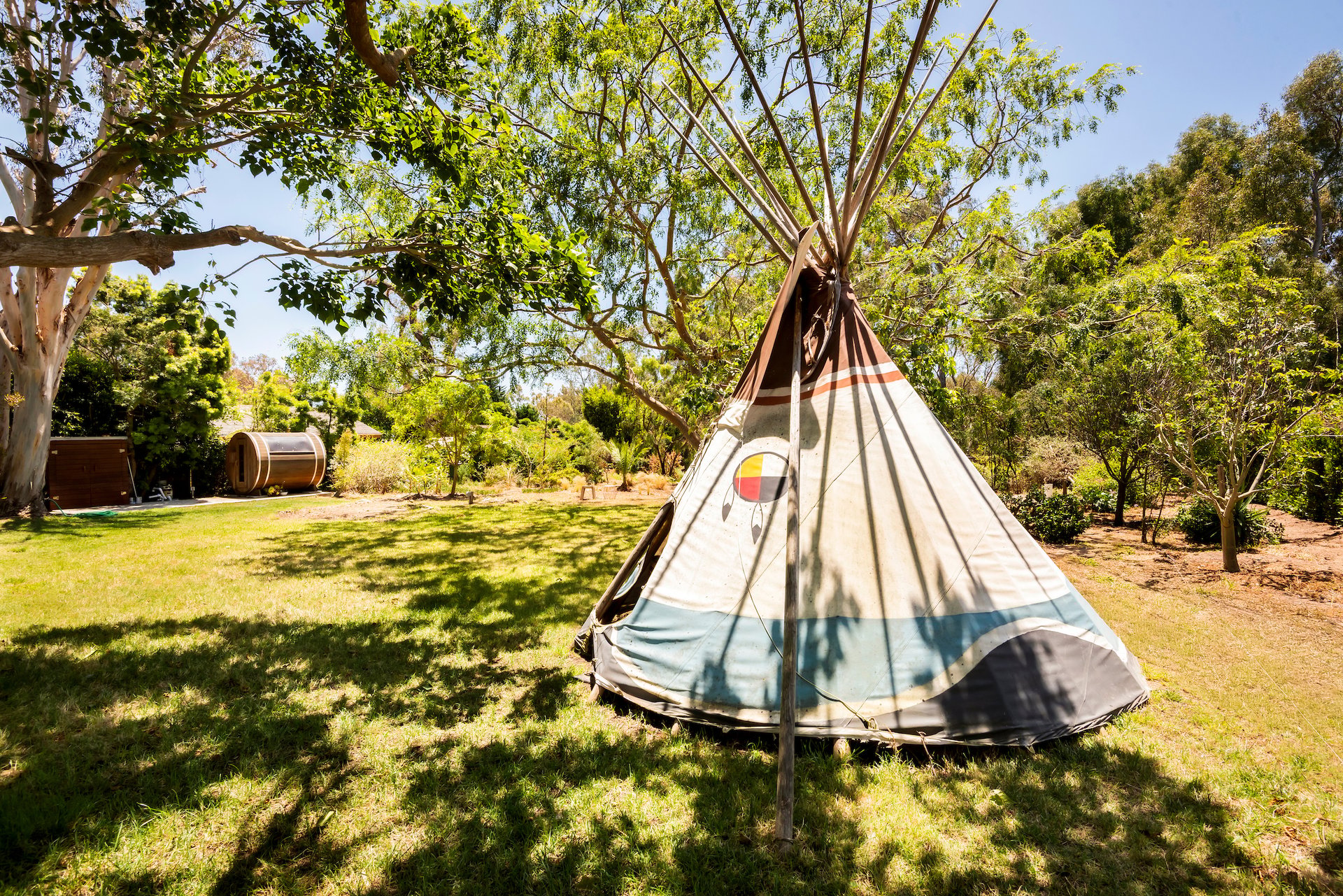 Shaded lawn with a canvas teepee and barrel-shaped sauna