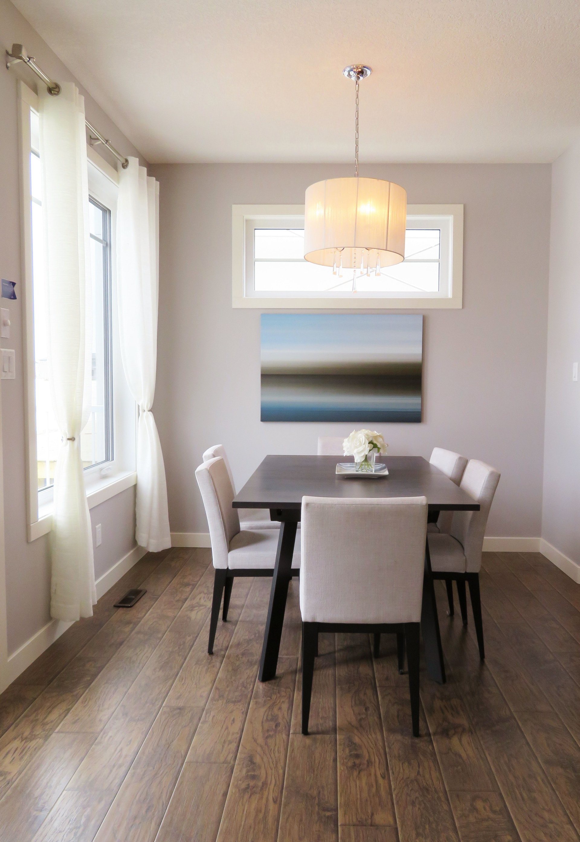 Dining room with a dark table, light upholstered chairs, and a large pendant light.
