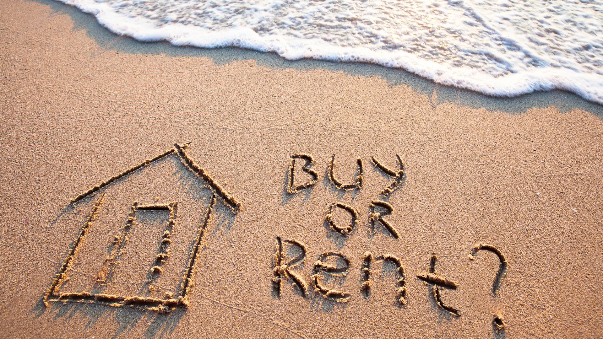 Buy or rent question written in sand on Miami beach with house drawing and ocean waves for The Edit Real Estate guide