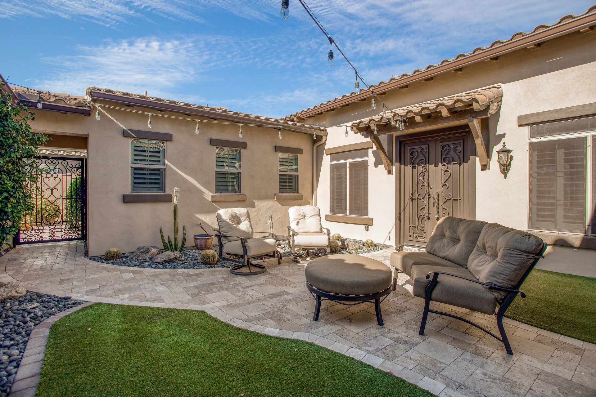 A Mediterranean-style courtyard patio with pavers, string lights, outdoor chairs, and a double-door entry.