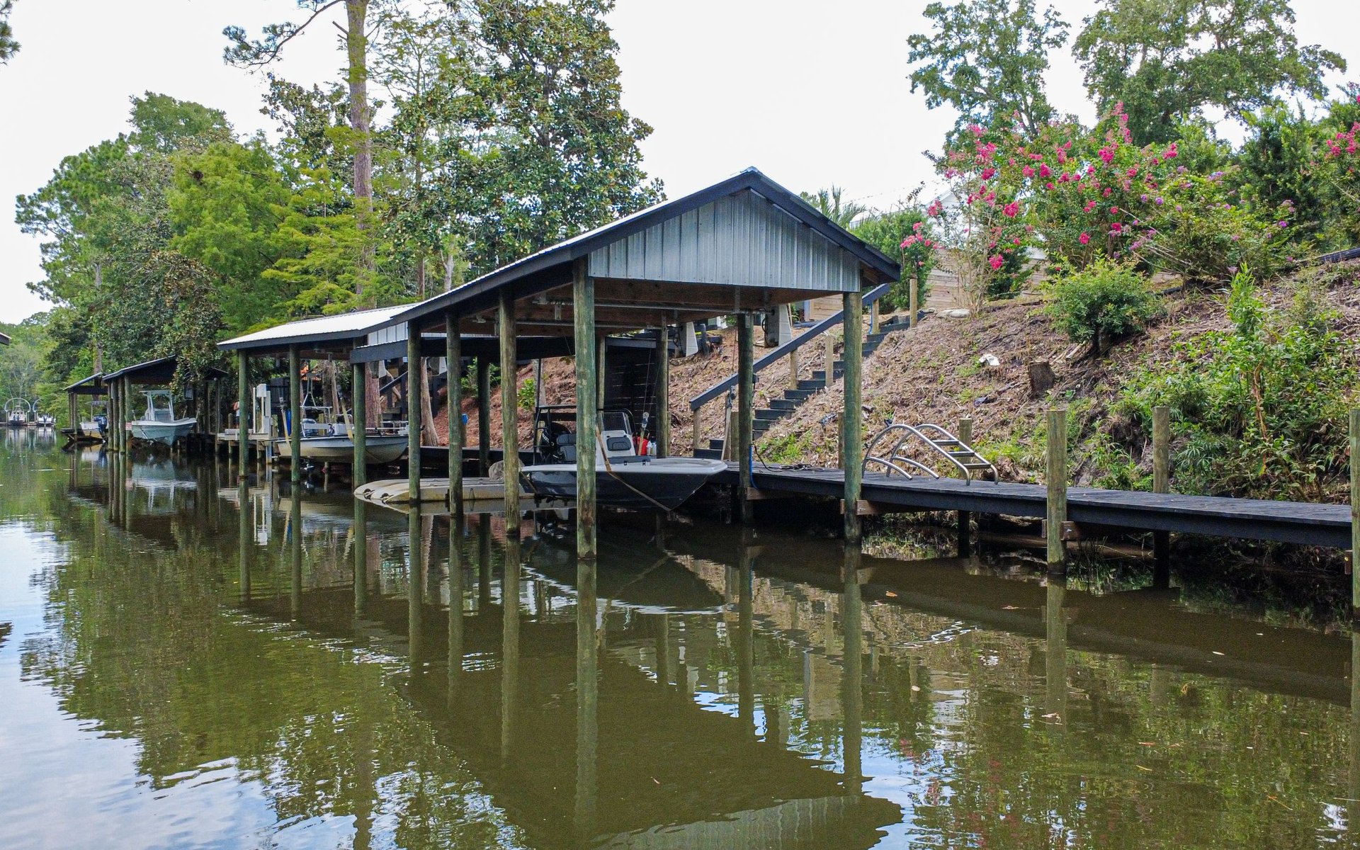 Covered boat slips and a wooden dock extend along a calm, tree-lined waterfront.
