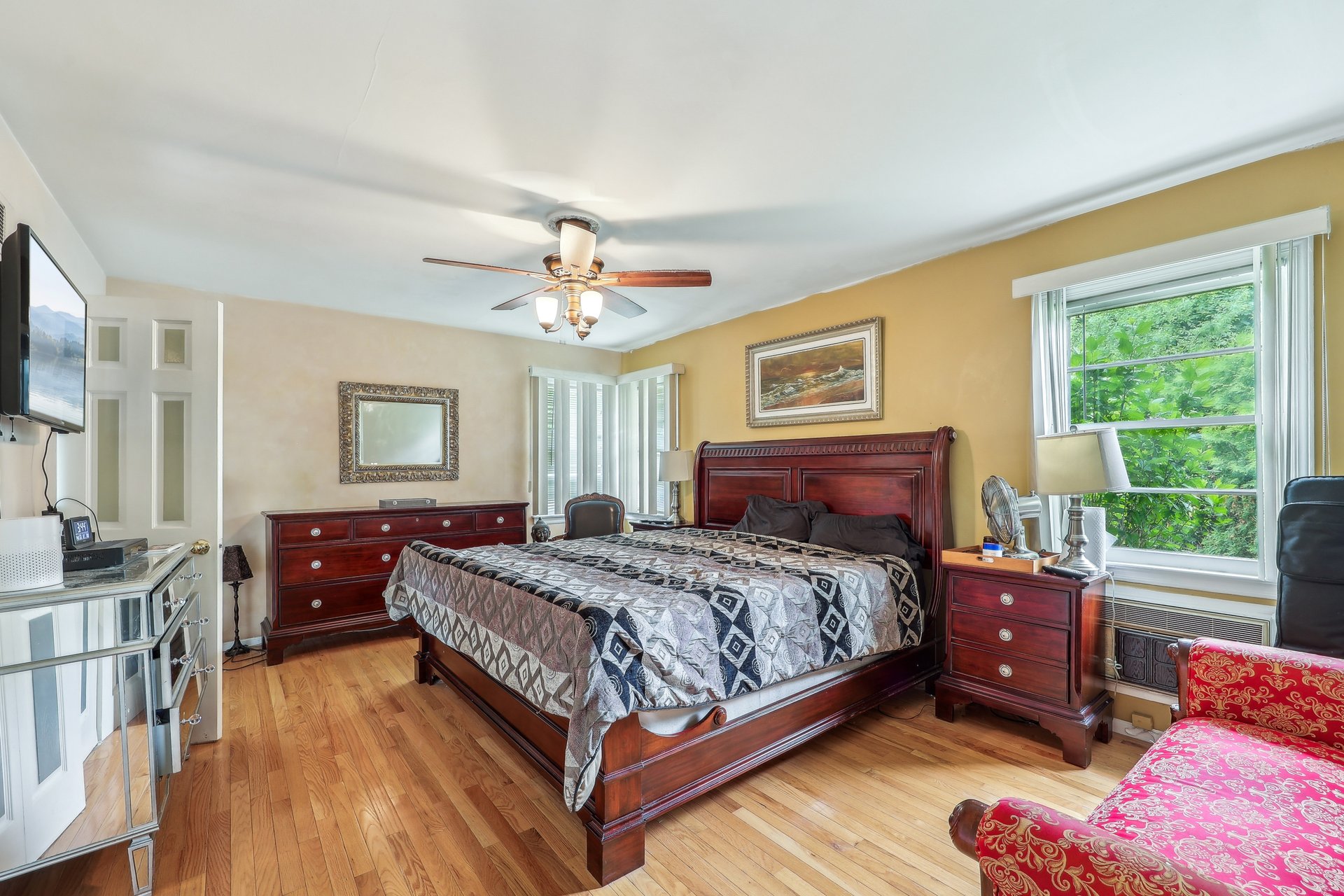 Bedroom with a large dark wood bed, hardwood floors, and windows overlooking greenery.