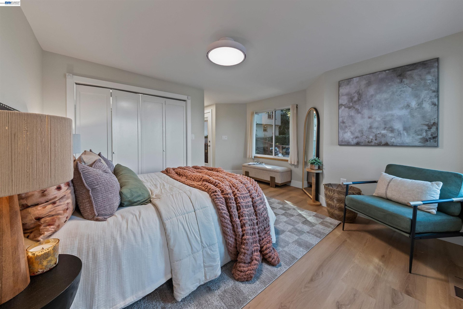 Staged bedroom with a white bed, rust-colored throw, and teal armchair.