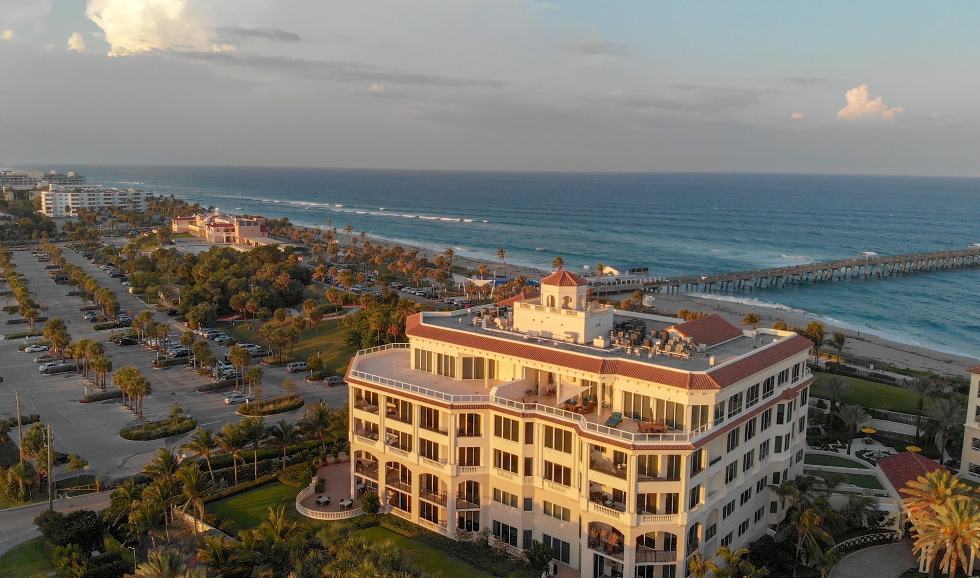 Beachfront condominium beside the Atlantic Ocean, with a long pier and palm-lined grounds.