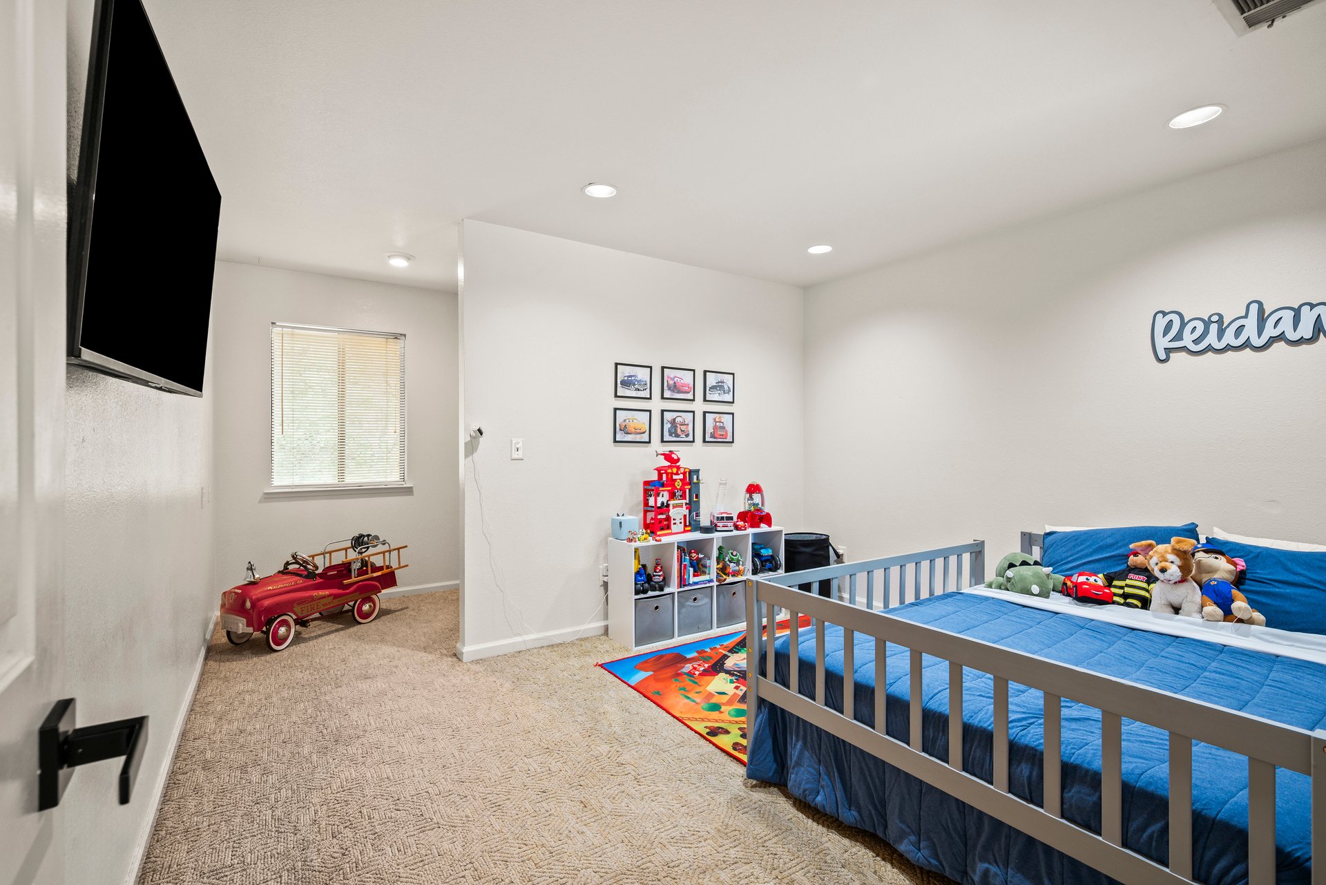 Child’s bedroom with a blue bed, toy storage, and a red ride-on fire truck.