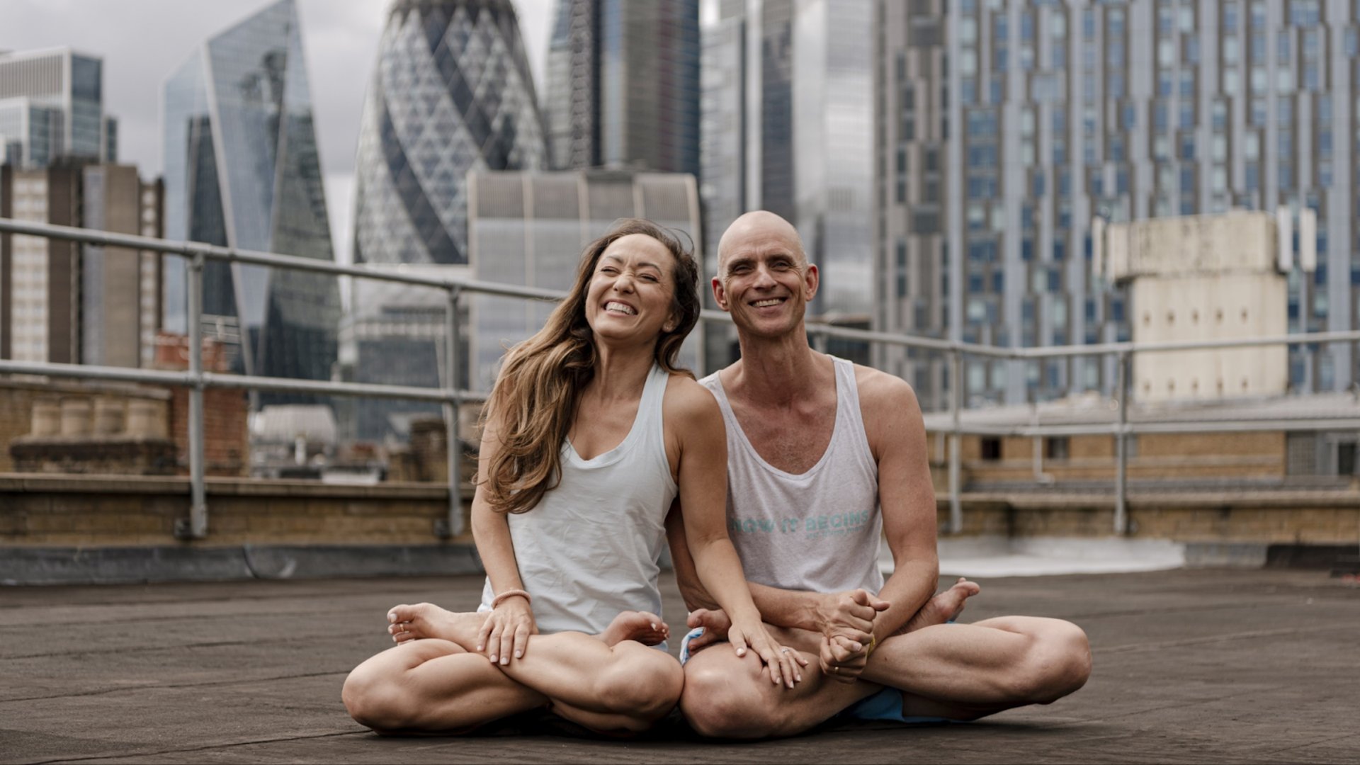 Happy couple meditating in lotus position on rooftop terrace with modern city skyline backdrop representing urban wellness lifestyle by The Edit Real Estate