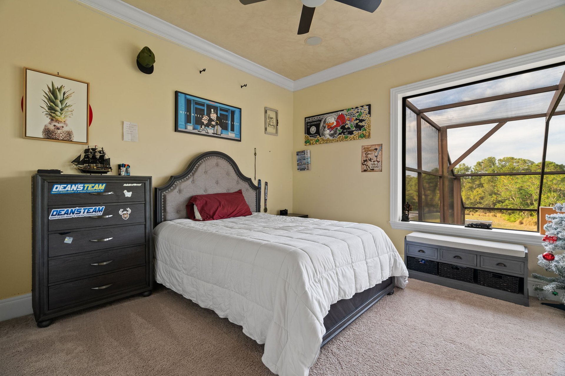 Bedroom with a large bed, dark wood dresser, and window overlooking a screened porch and trees.