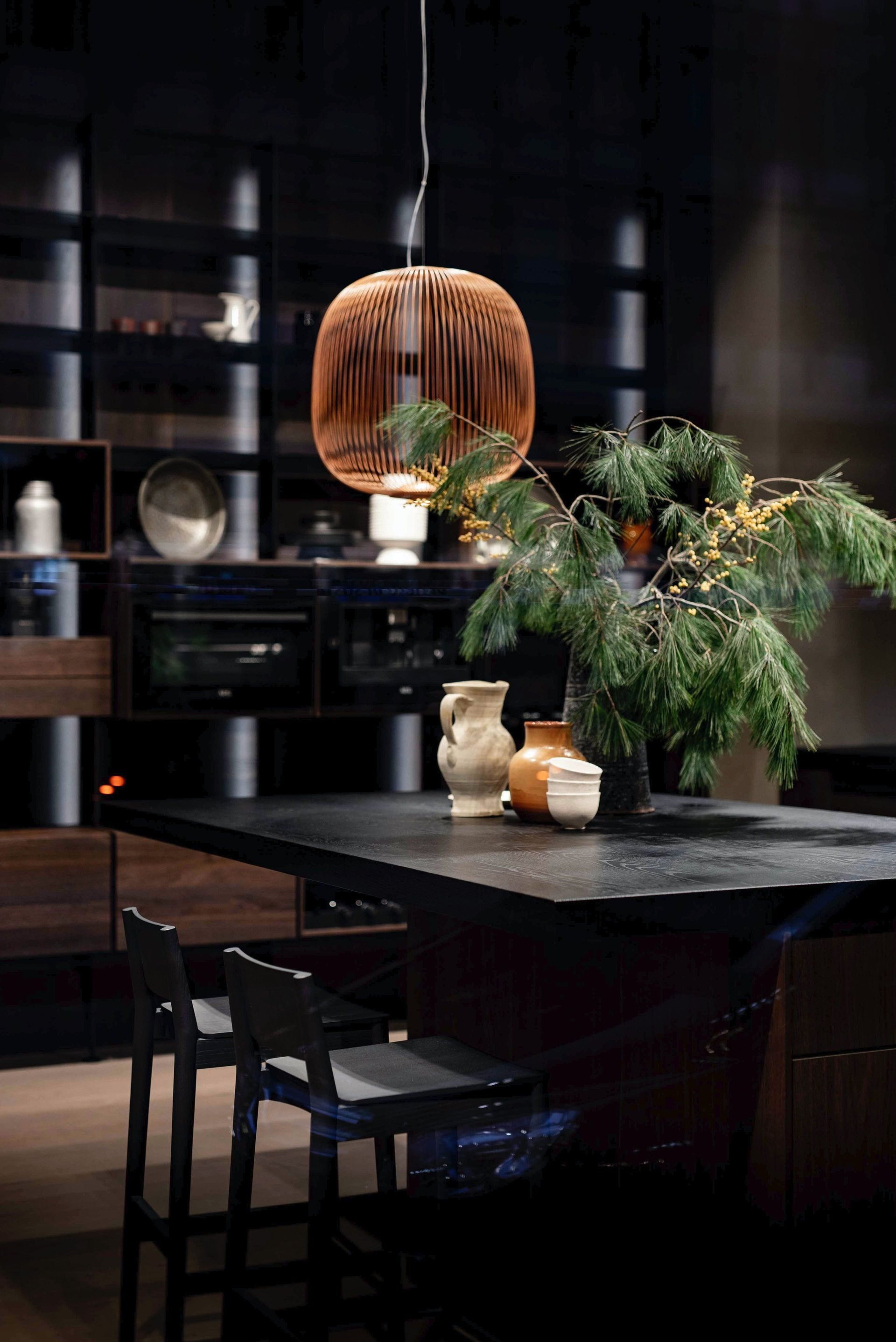 Modern dark kitchen with a wooden pendant light and leafy branches arranged on the island.