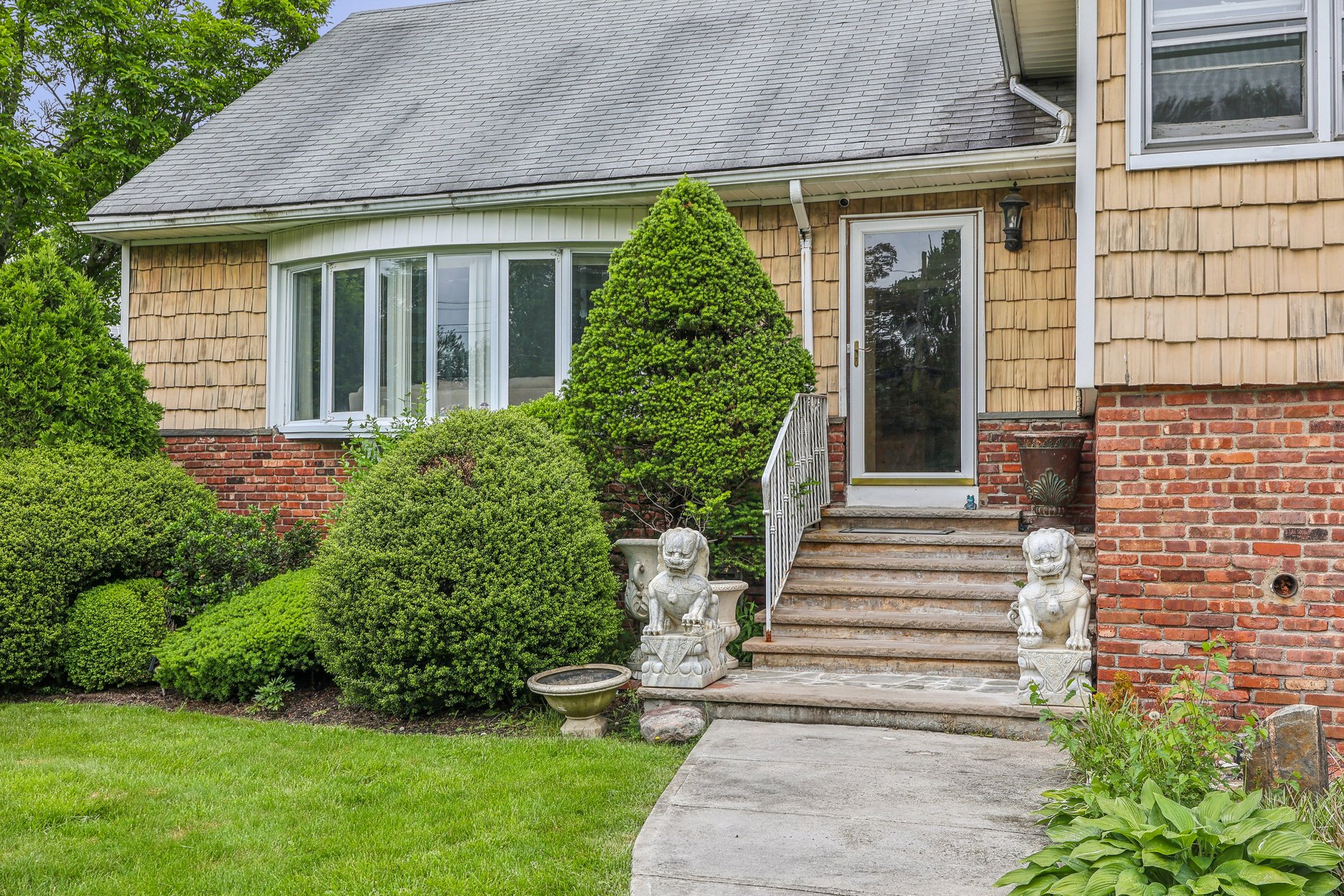 House entrance with stone steps, landscaped shrubs, and lion statues flanking the doorway.