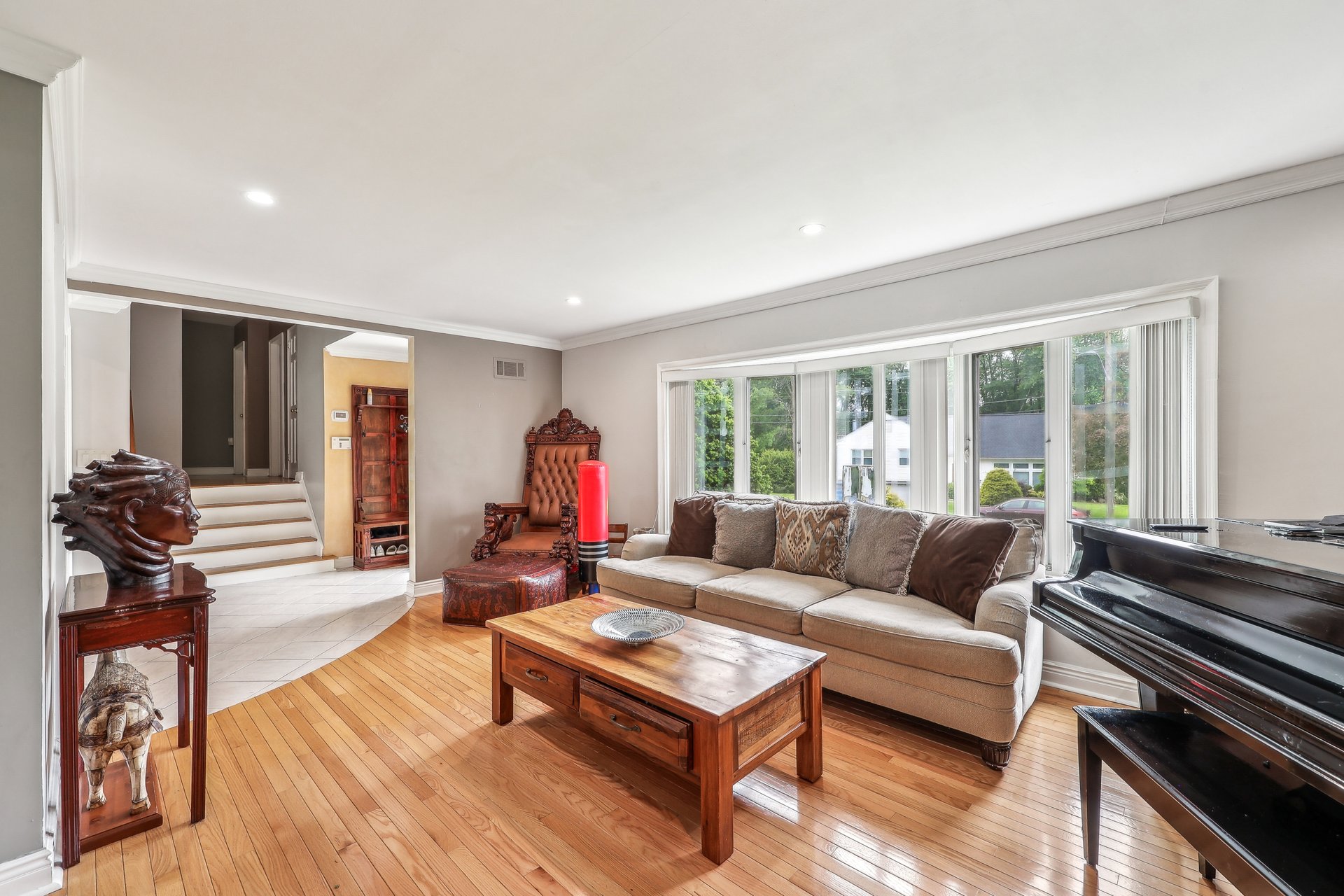 Living room with hardwood floors, a beige sectional, large windows, and a black grand piano.
