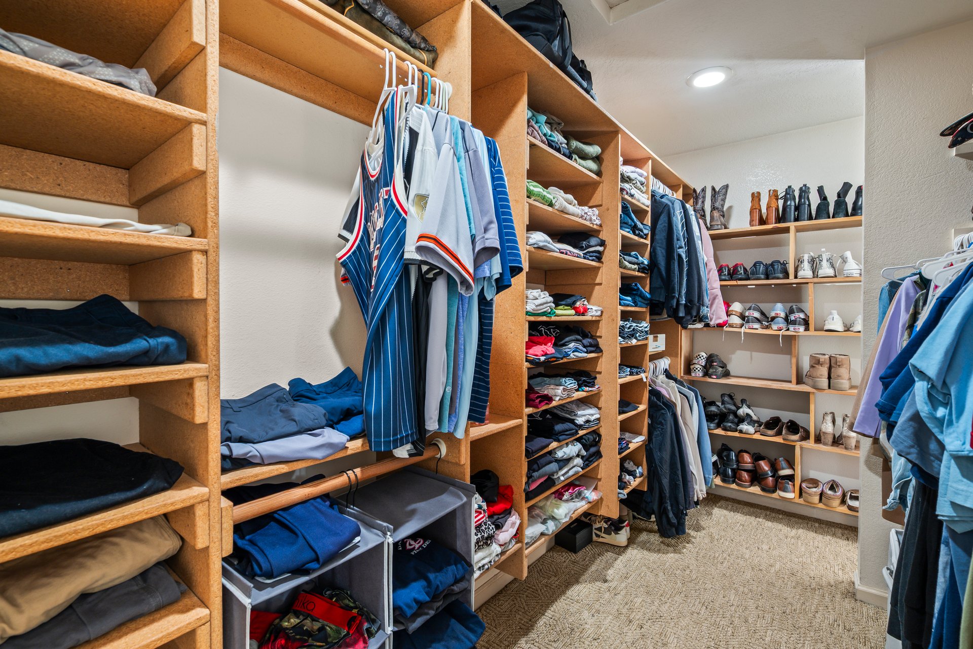 Walk-in closet with extensive wooden shelving, hanging clothes, folded garments, and rows of shoes.