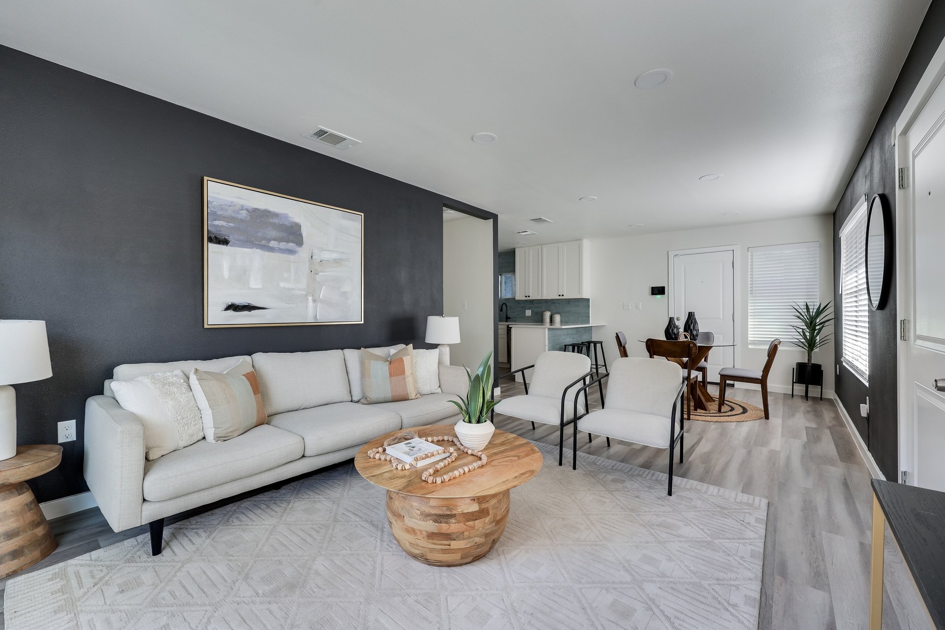 Staged living room with a white sofa, charcoal accent wall, and open kitchen and dining area.