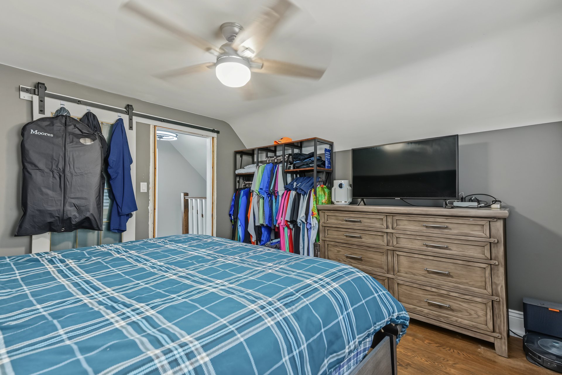 Bedroom with a blue plaid bedspread, clothing racks, and a television on a wooden dresser.