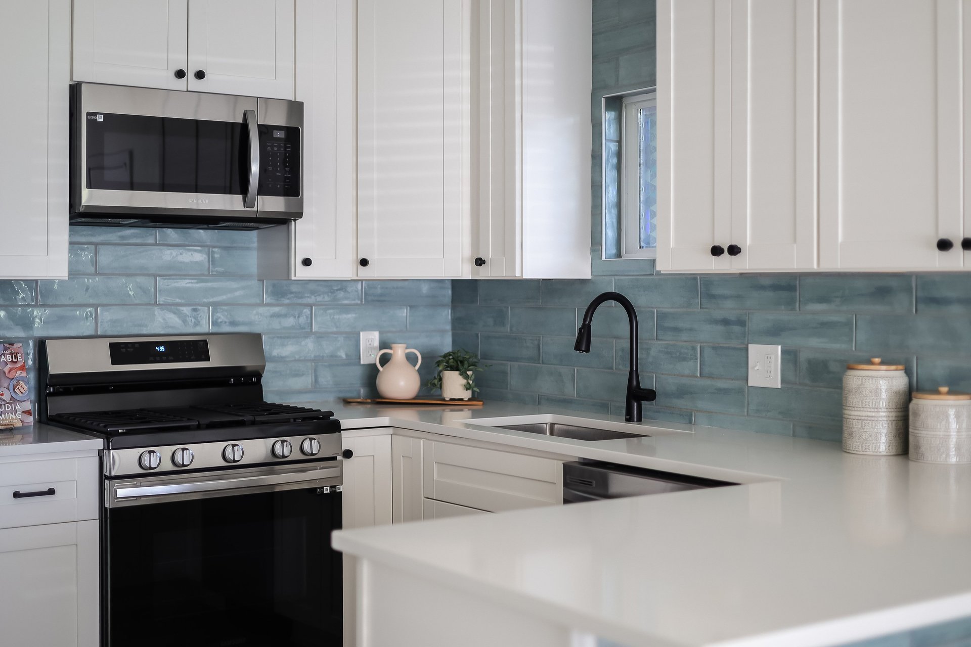 Kitchen with white cabinets, blue-gray tile backsplash, black gas range, and farmhouse-style sink.