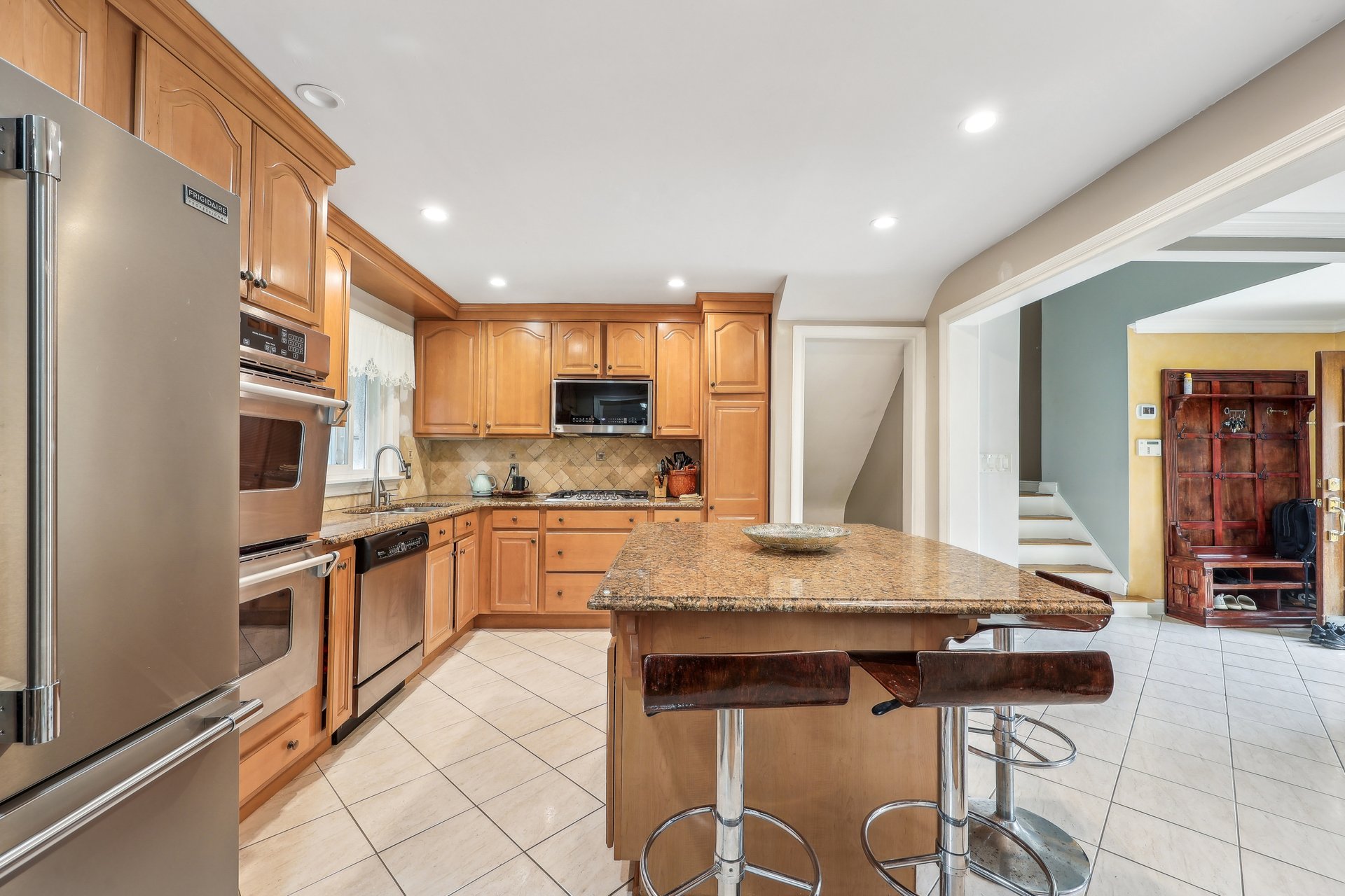 Kitchen with wood cabinetry, stainless steel appliances, and a granite island with bar stools.