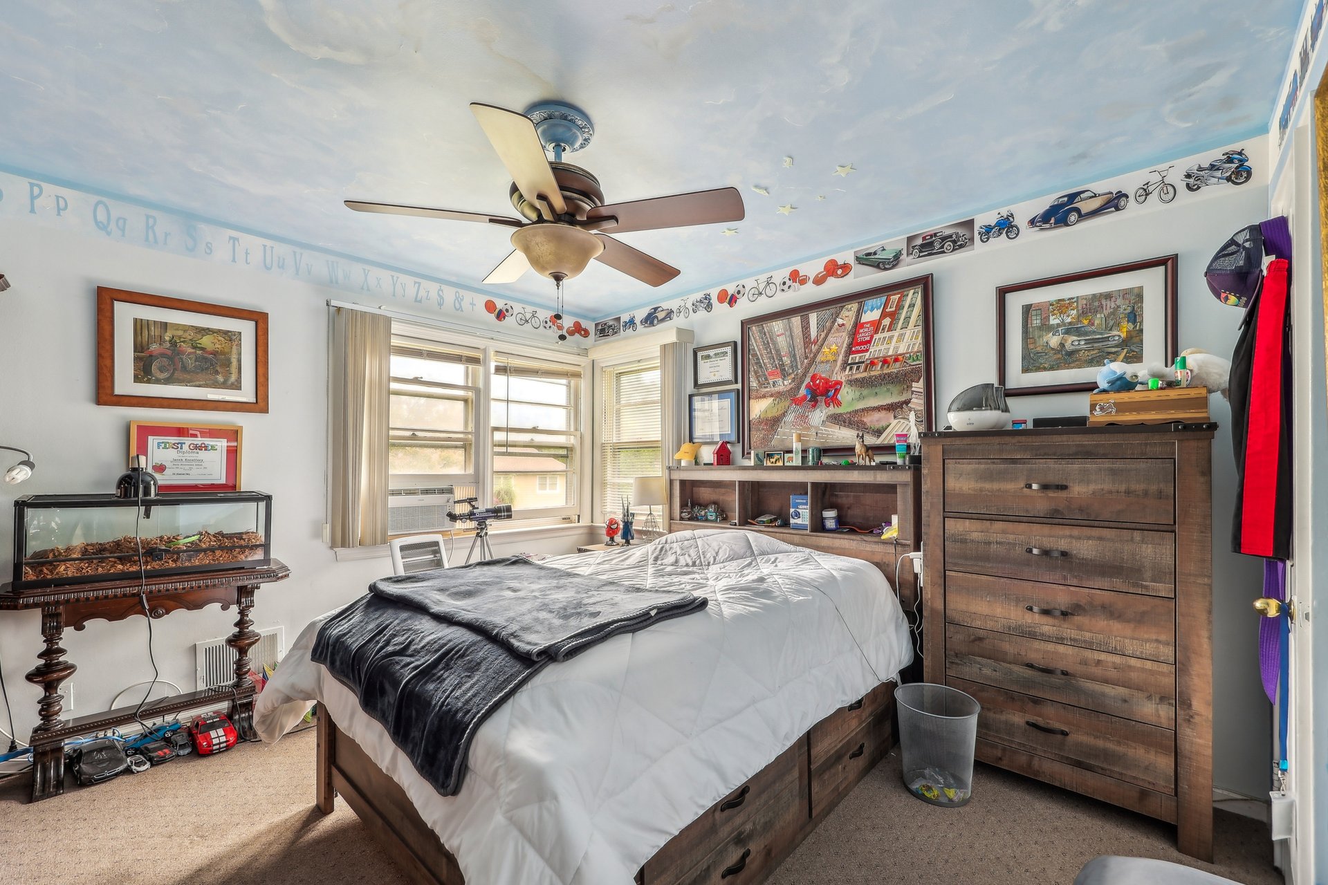 Bedroom with a large wooden bed, bright windows, and vehicle-themed decorations along the walls.