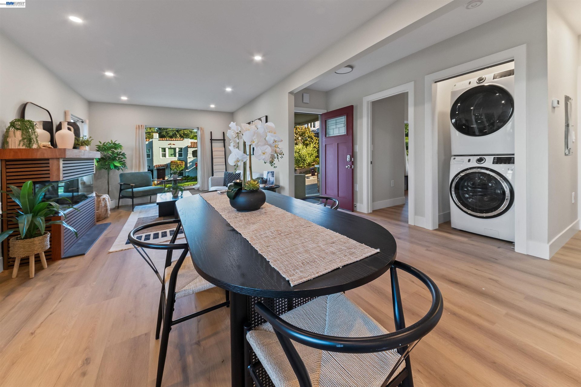 Dining area with a long dark table, light wood floors, and a stacked washer and dryer by the entry.