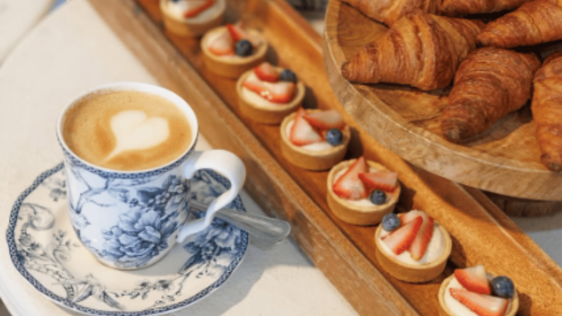 Gourmet breakfast with latte art heart design, fresh croissants and berry tarts on wooden tray representing upscale lifestyle near The Edit Real Estate luxury properties