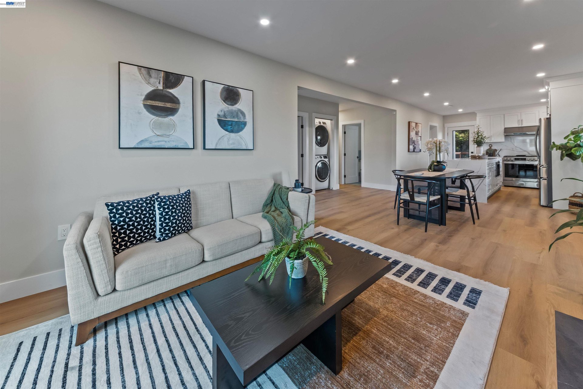 Open-plan living room and kitchen with a gray sofa, patterned rugs, and white cabinetry.