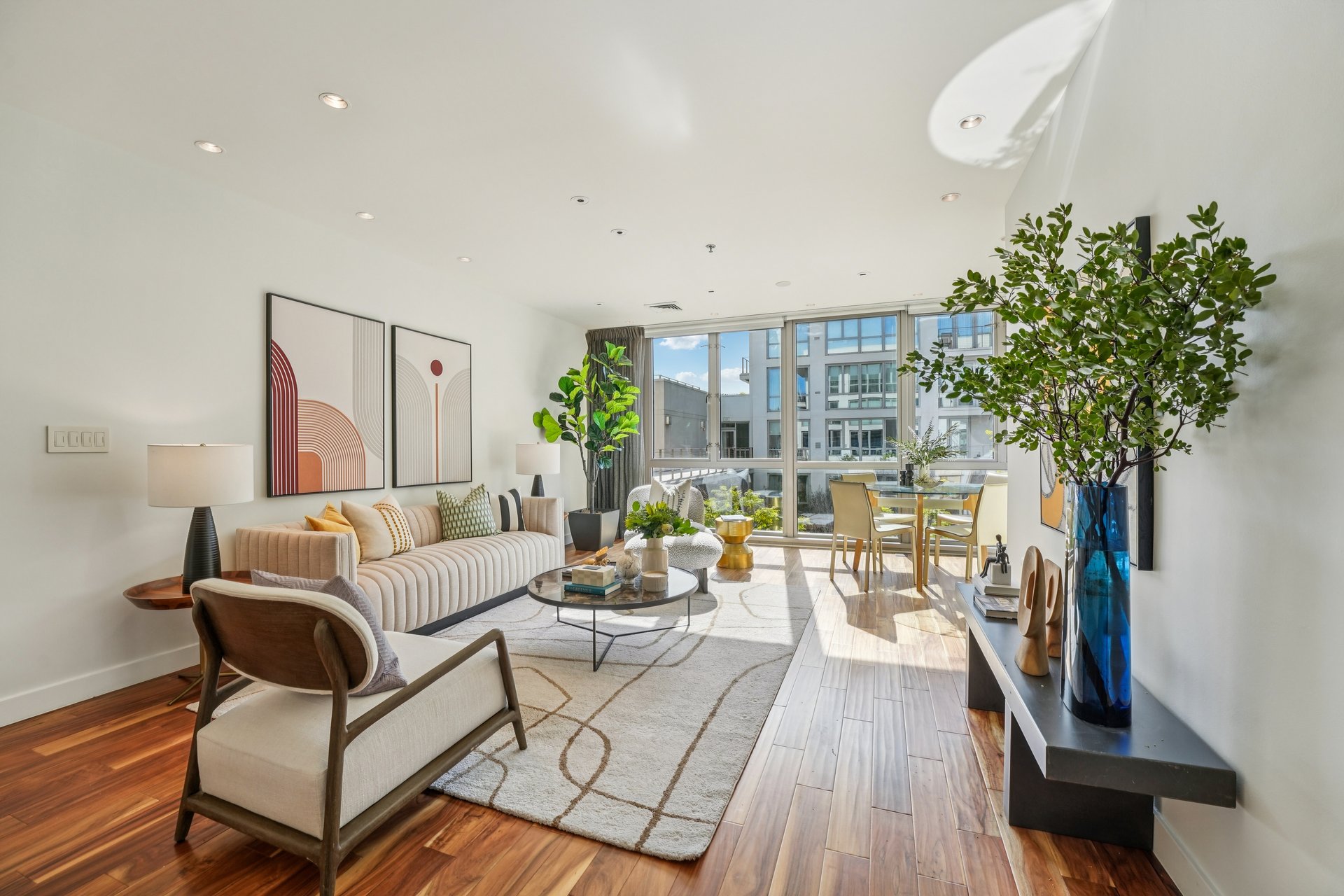 Bright staged living room with furniture, artwork, and large windows