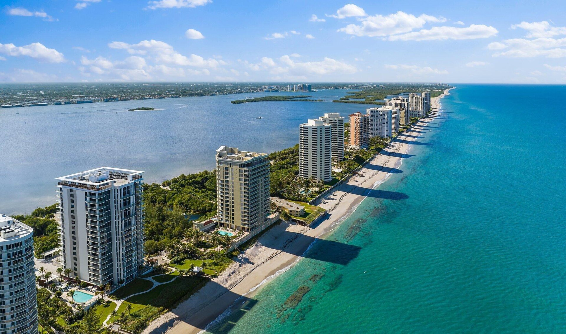 Aerial panorama of beachfront high-rises between the Atlantic Ocean and an inland waterway.