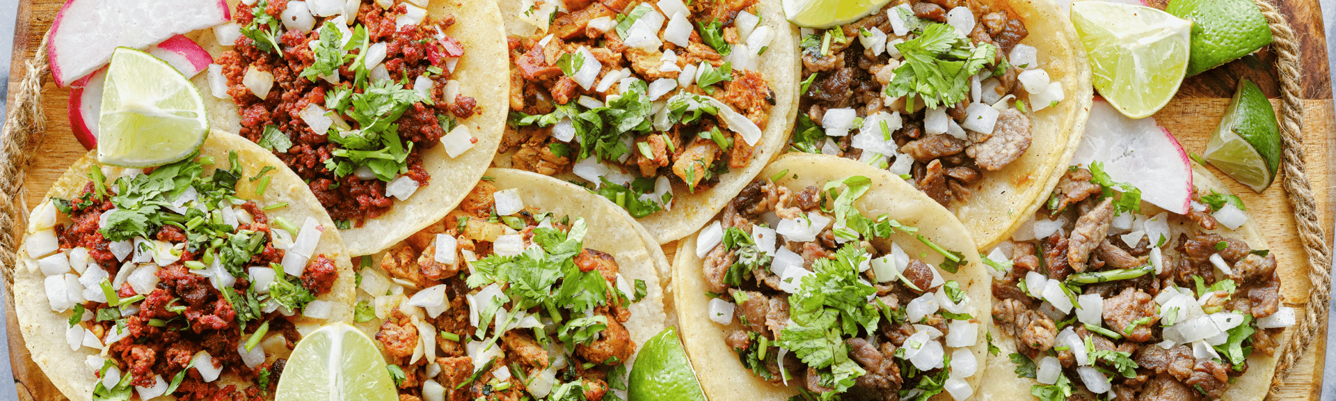 A platter of assorted tacos topped with cilantro, onions, and lime wedges, served with radish slices.