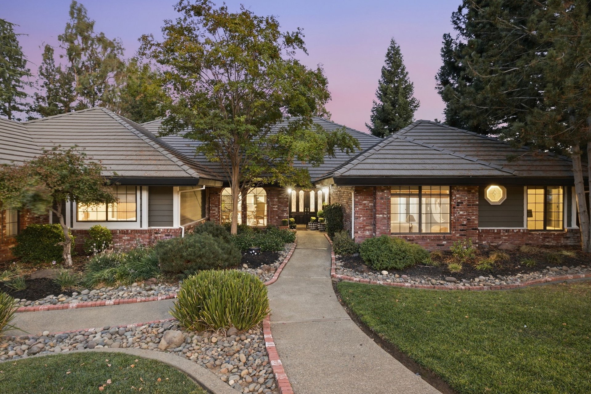 Single-story brick-and-siding home with a tiled roof and curved front walkway at dusk.