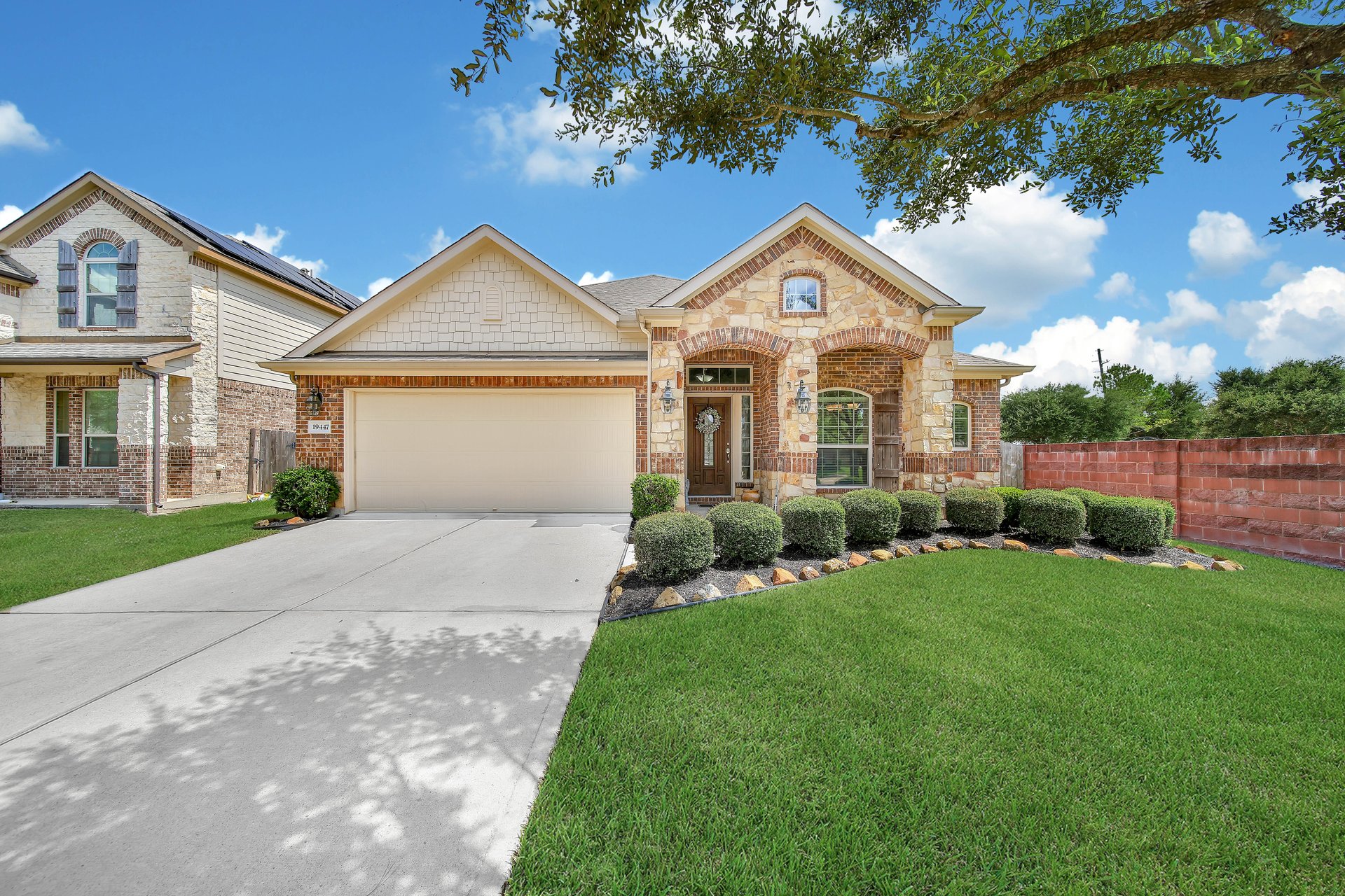 Stone-and-brick home with a two-car garage, landscaped front lawn, and wide driveway.