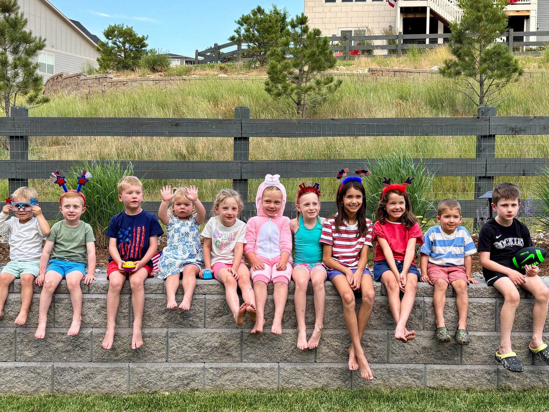 Eleven children sit together on a stone wall, several wearing festive headbands and one dressed as a pink bunny.