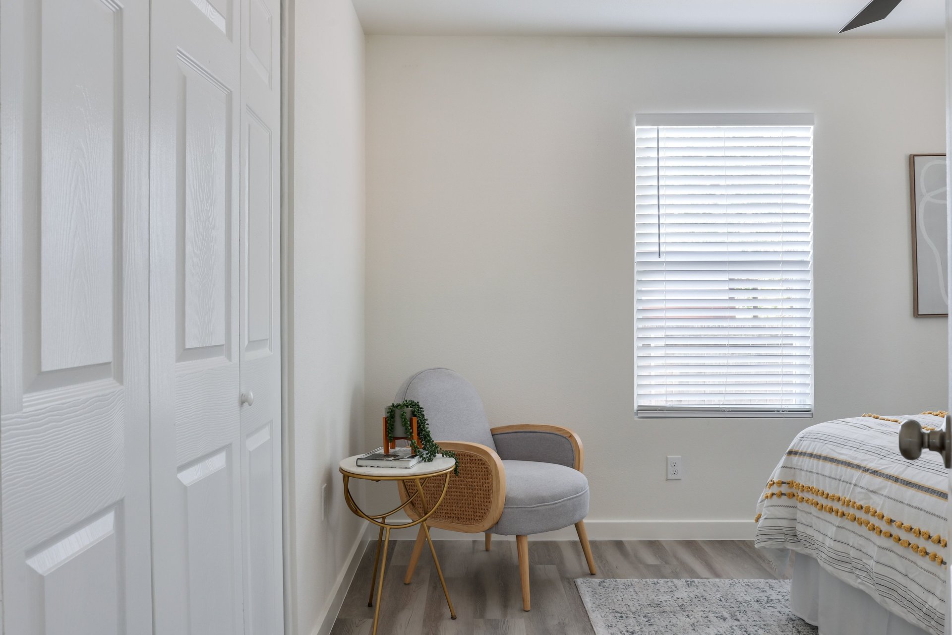 Bedroom with white closet doors, a gray accent chair, and a bed beside a window with blinds.