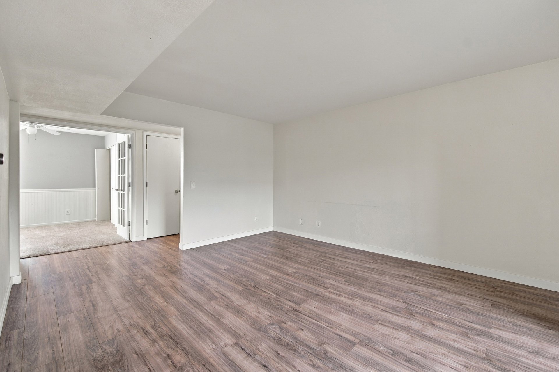 Empty room with wood-look flooring and a doorway to a carpeted room.