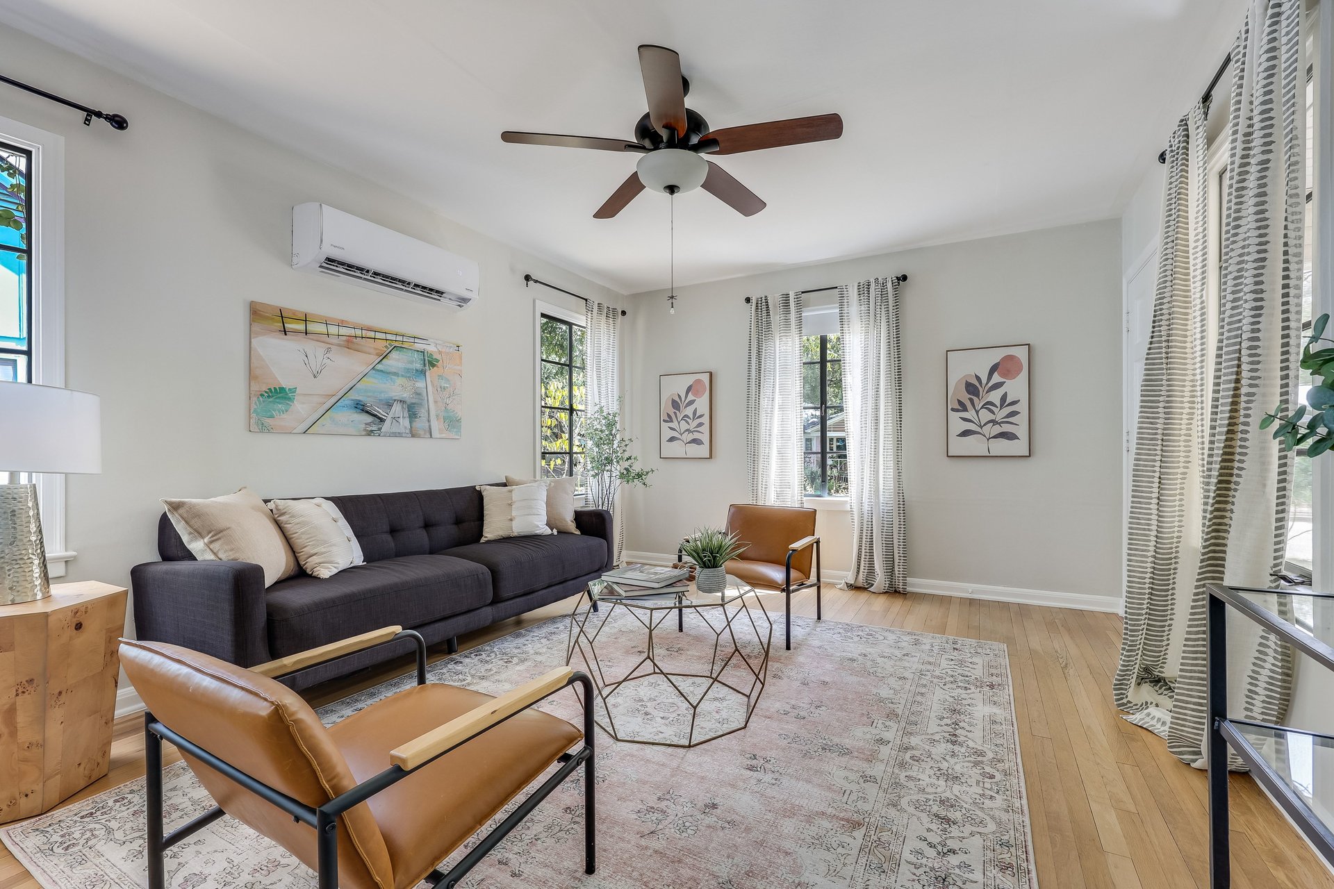 Living room with a charcoal sofa, tan leather chairs, patterned rug, and tall curtained windows.