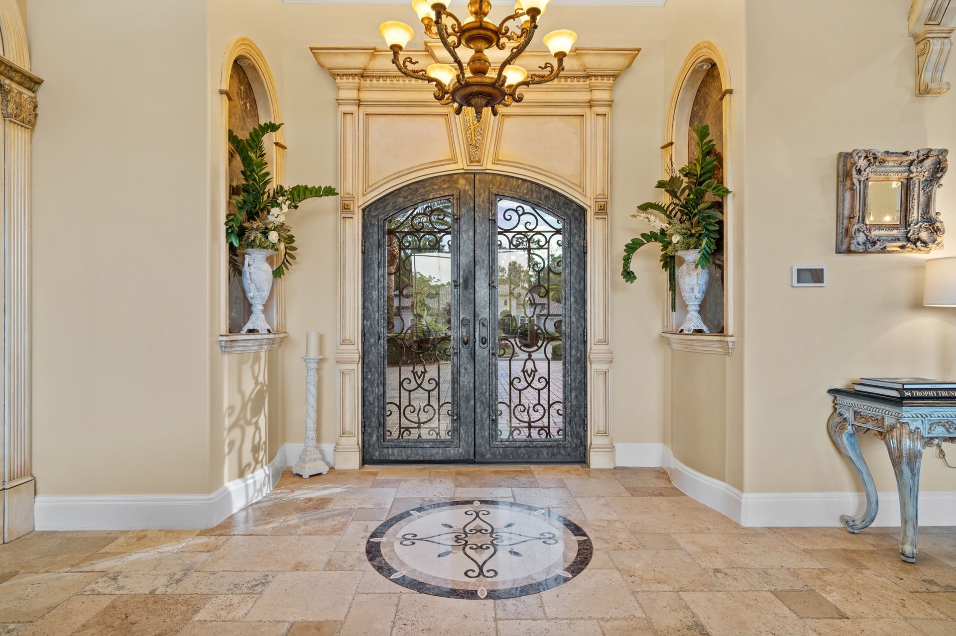 Foyer with ornate ironwork double doors, a chandelier, and a circular floor mosaic.
