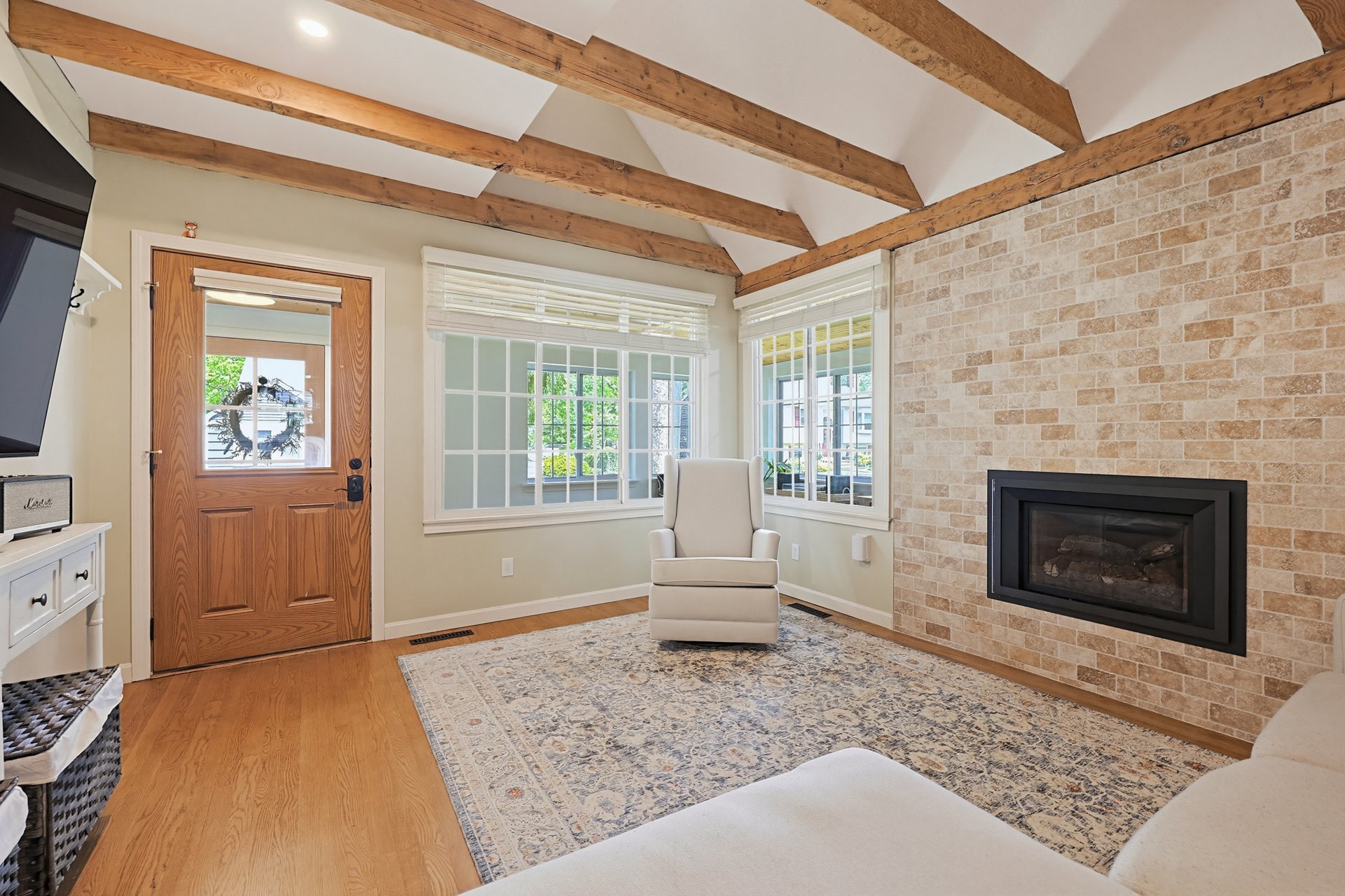 Living room with exposed timber beams, a stone fireplace wall, and large windows.