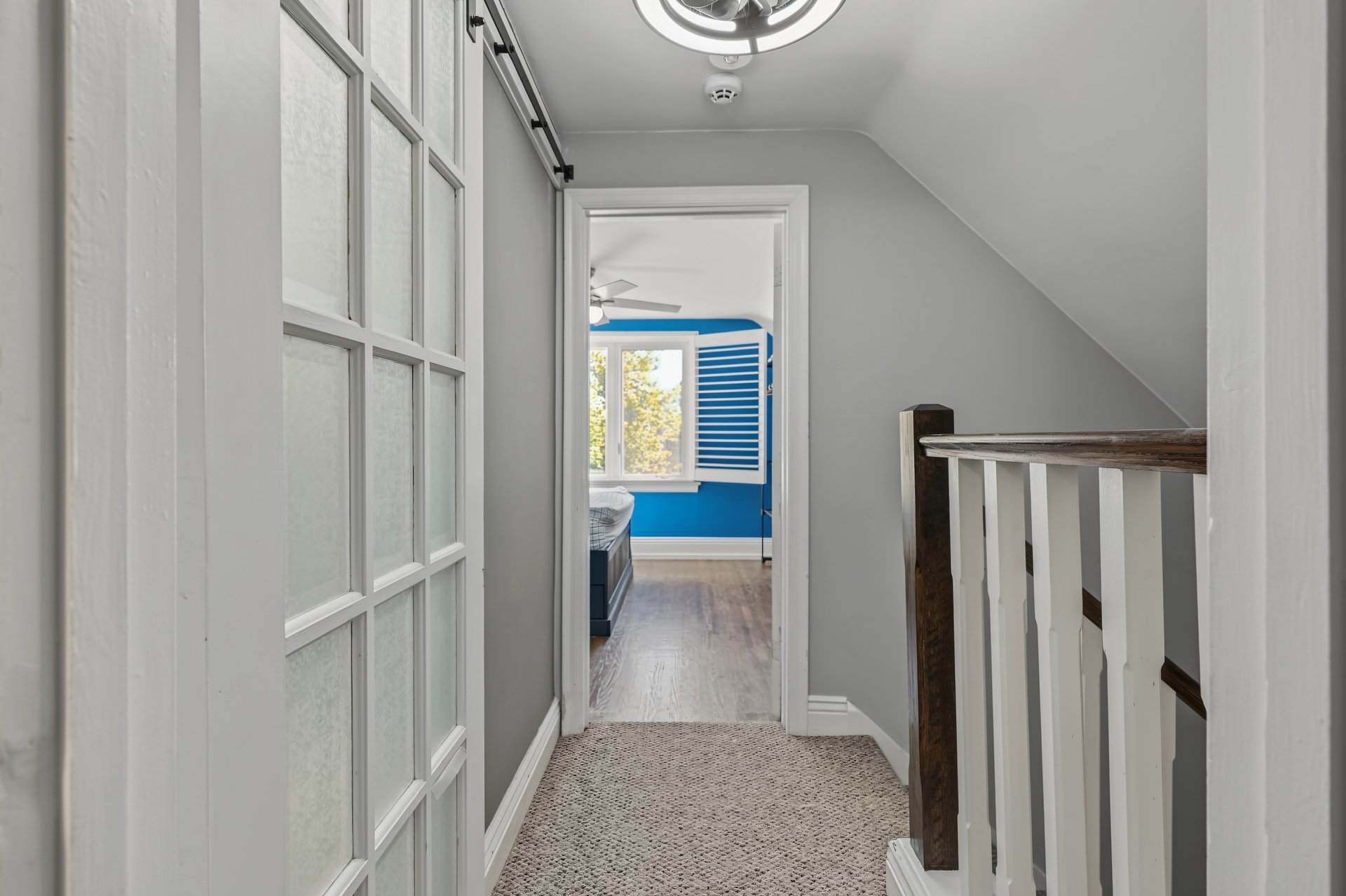 Upstairs hallway with patterned carpet and dark wood railing, opening to a bedroom with a bright blue wall.