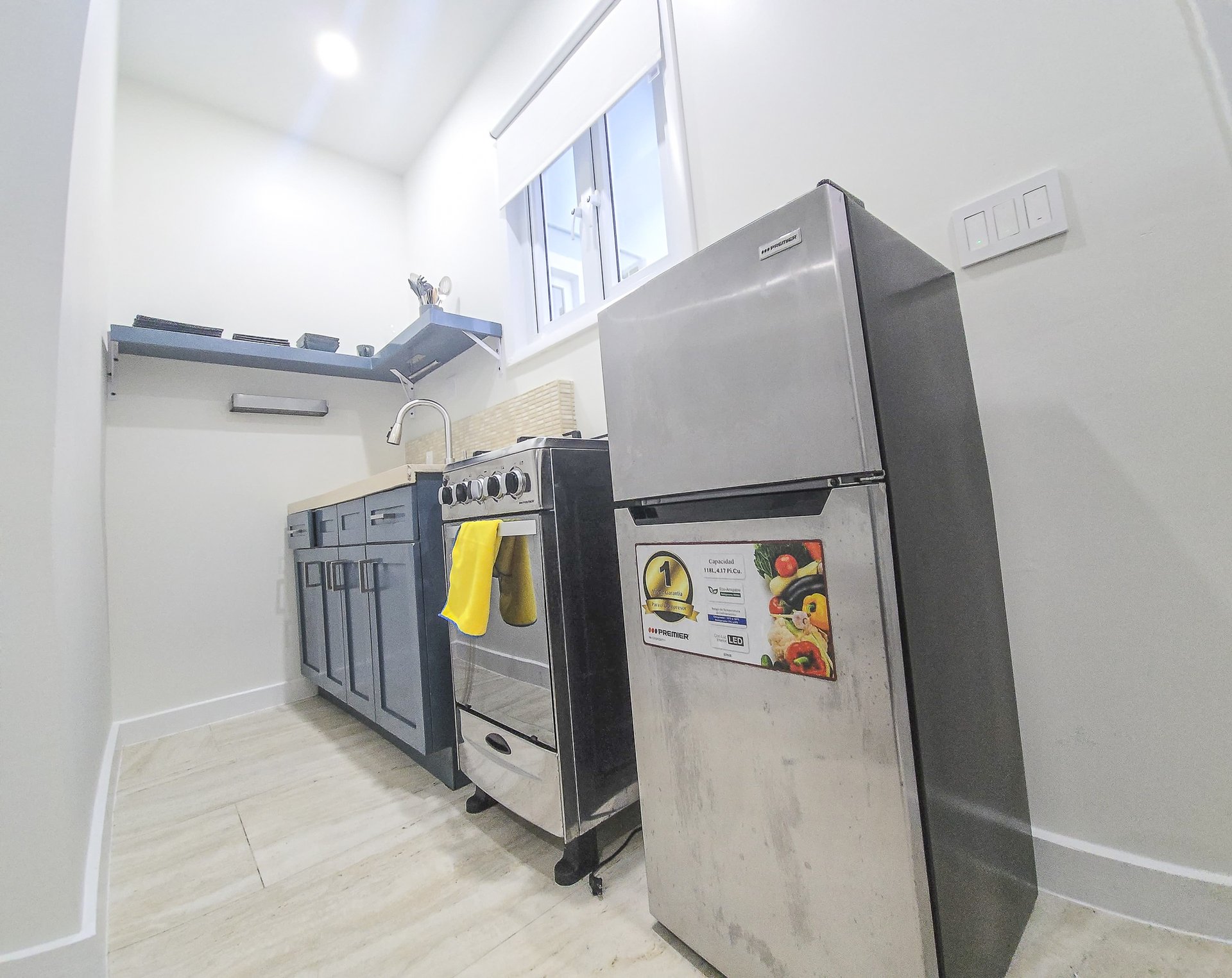 Compact kitchen with dark blue cabinets, stainless-steel stove and refrigerator, and a small high window.