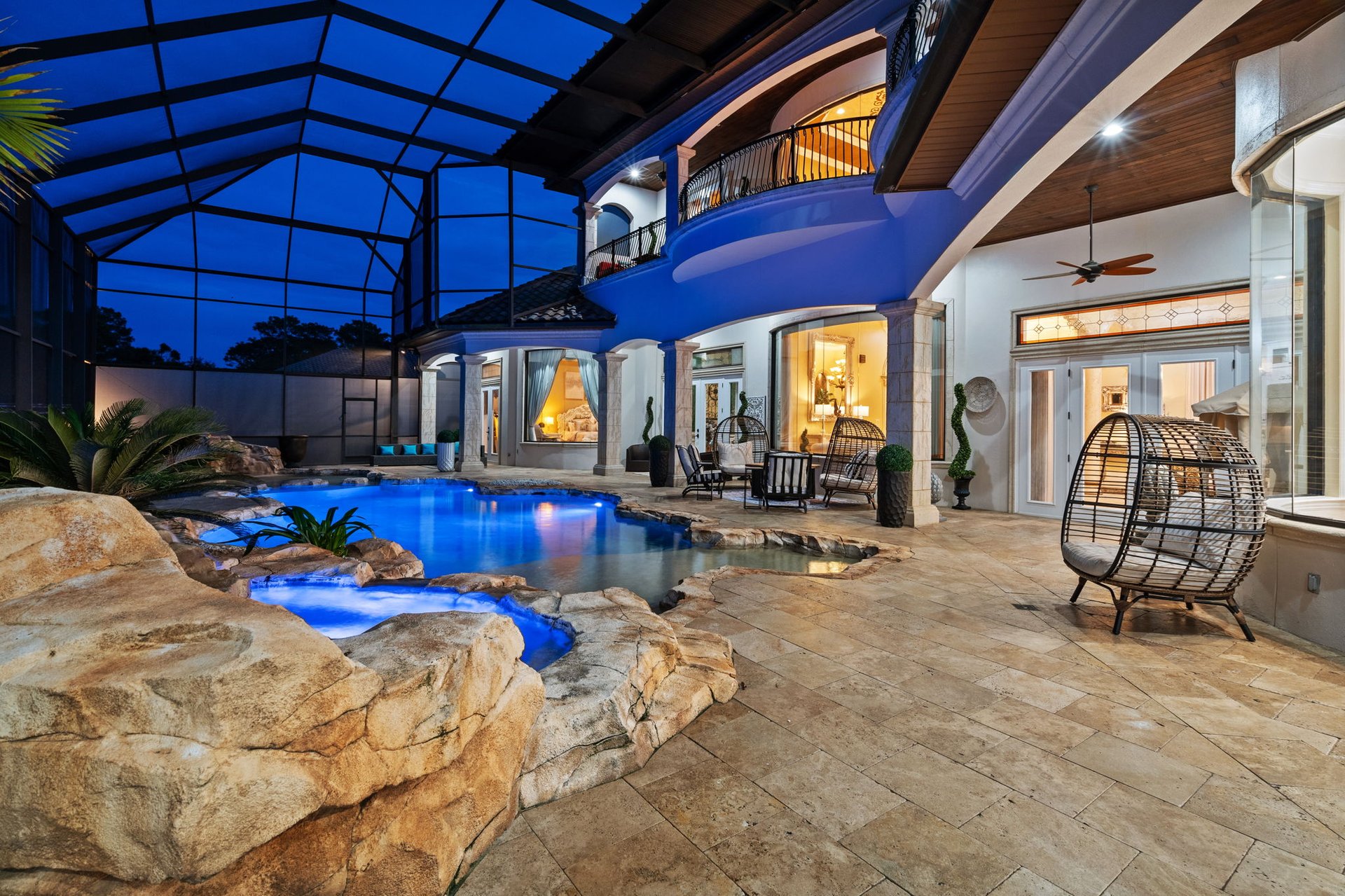 Backyard pool beside a covered patio, with rock edging and a two-story home.