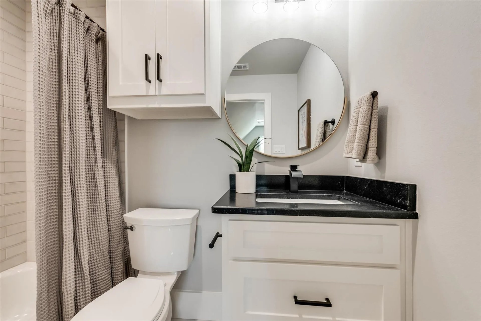 Bathroom with a black countertop, round mirror, and gray shower curtain.