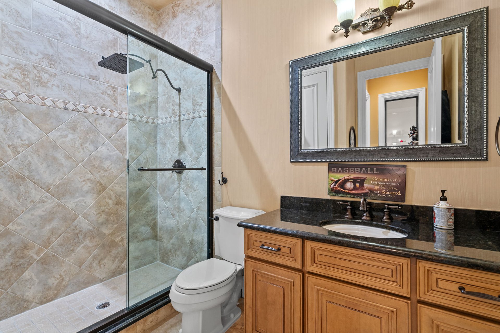 Bathroom with a tiled glass shower, toilet, and wood vanity beneath a large framed mirror.