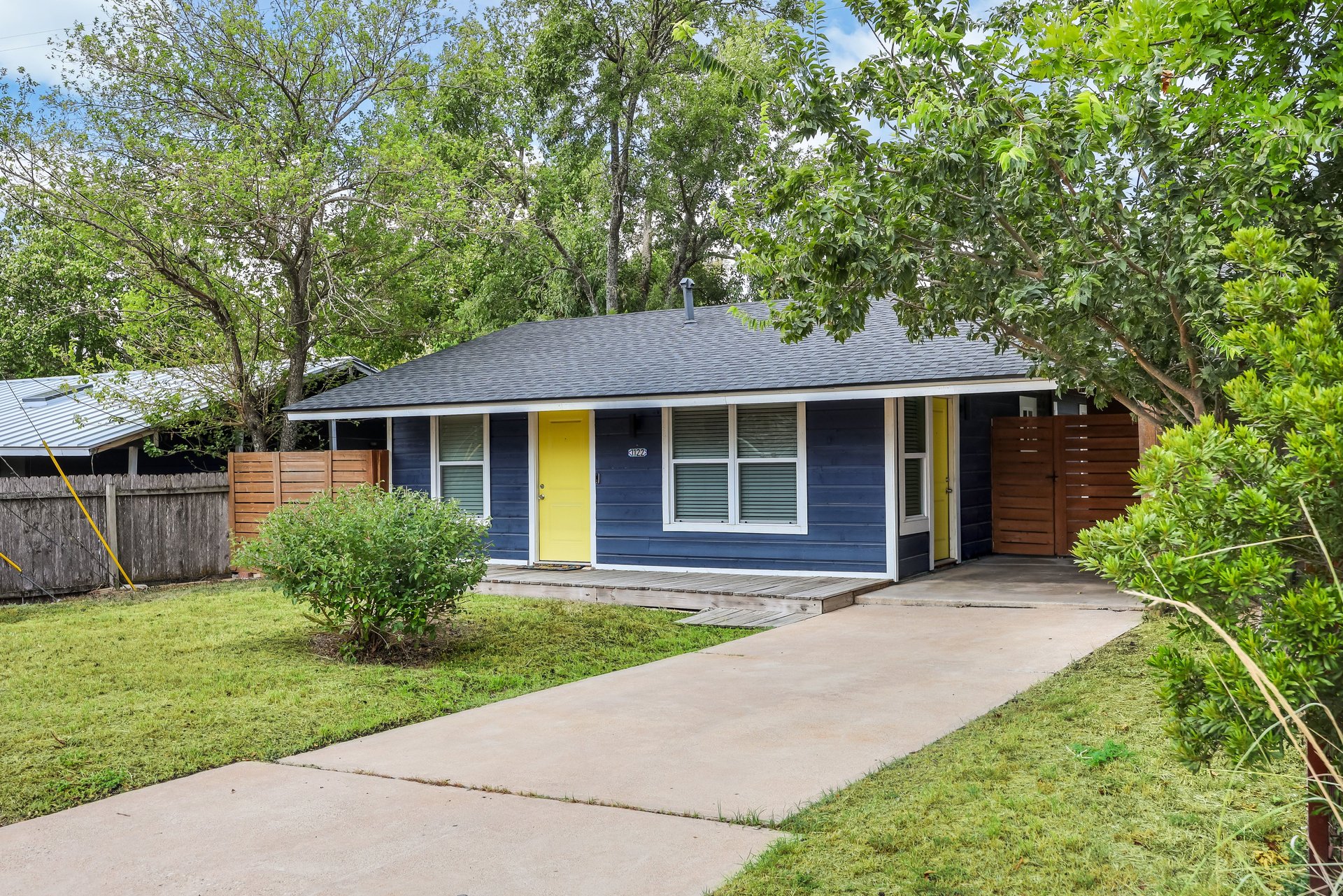 Blue single-story house with yellow doors, white-trimmed windows, and a wide concrete driveway.