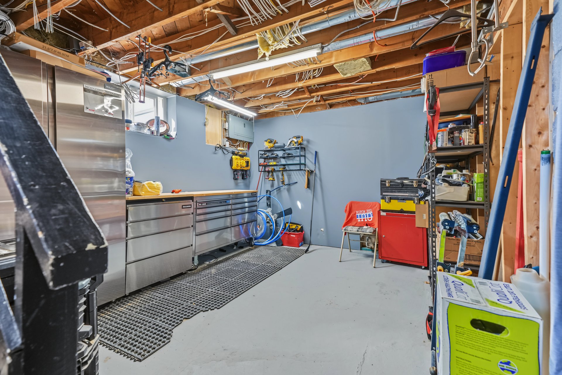 Basement workshop with stainless steel cabinets, wall-mounted tools, and a red tool chest.