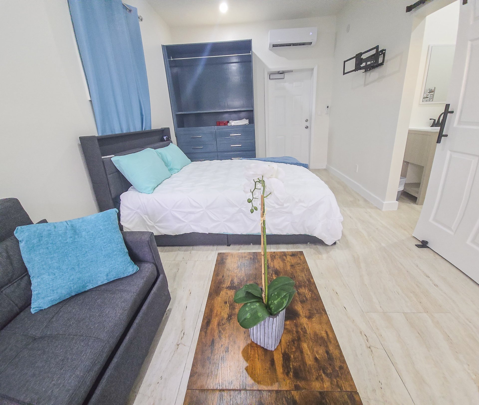 Furnished bedroom with a white bed, blue wardrobe, and gray seating area.