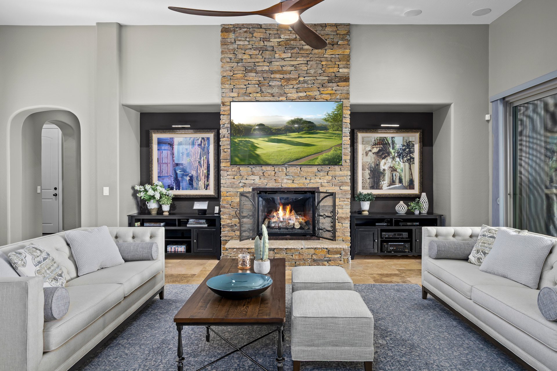 Staged living room with two sofas facing a coffee table and stone fireplace with TV above.