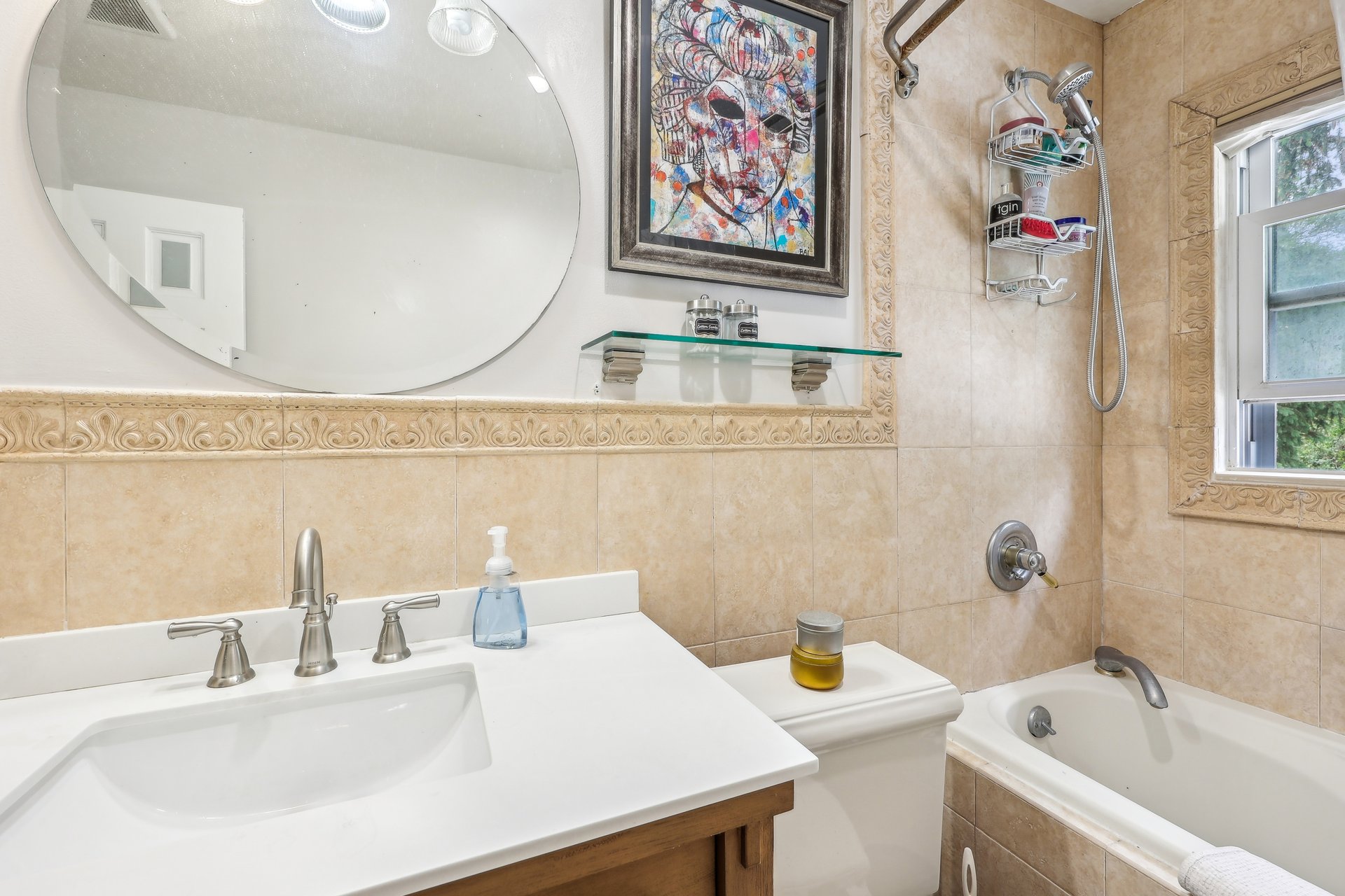 Bathroom with a white vanity, oval mirror, beige decorative tile, bathtub, and window.