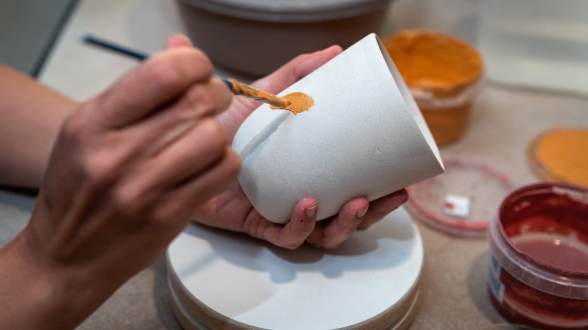 Hands painting handmade ceramic bowl with earth-tone glazes - The Edit Real Estate Miami artisan home decor