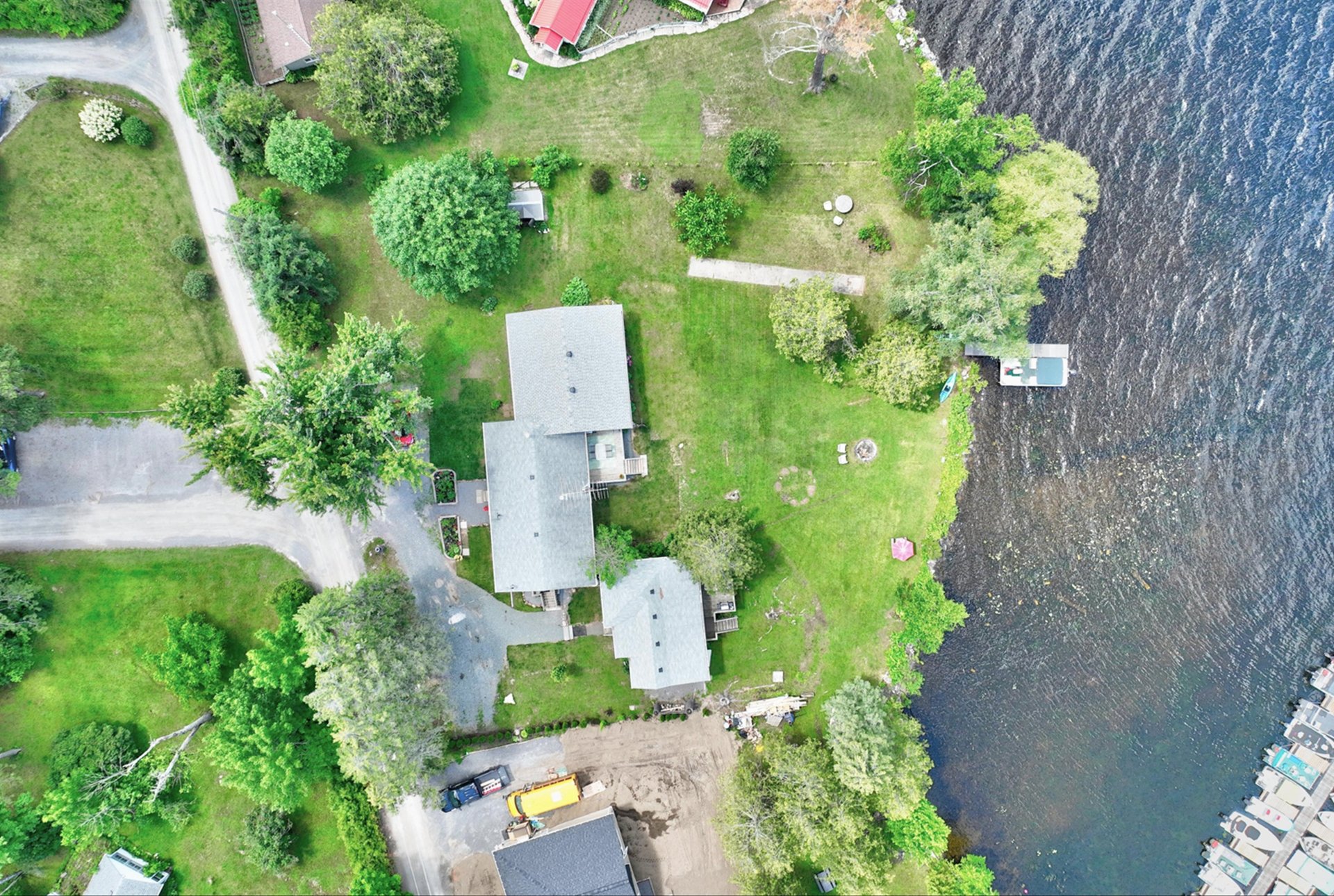 Aerial view of a lakeside house on a grassy, tree-lined lot with a dock.