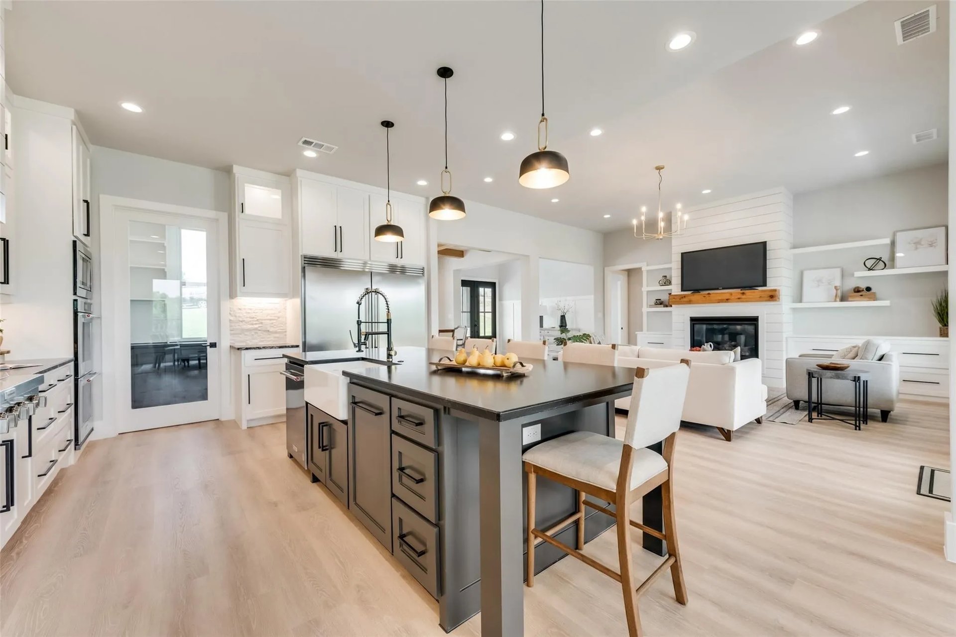 Open kitchen with a large dark island, white cabinetry, and an adjoining living area with a fireplace.