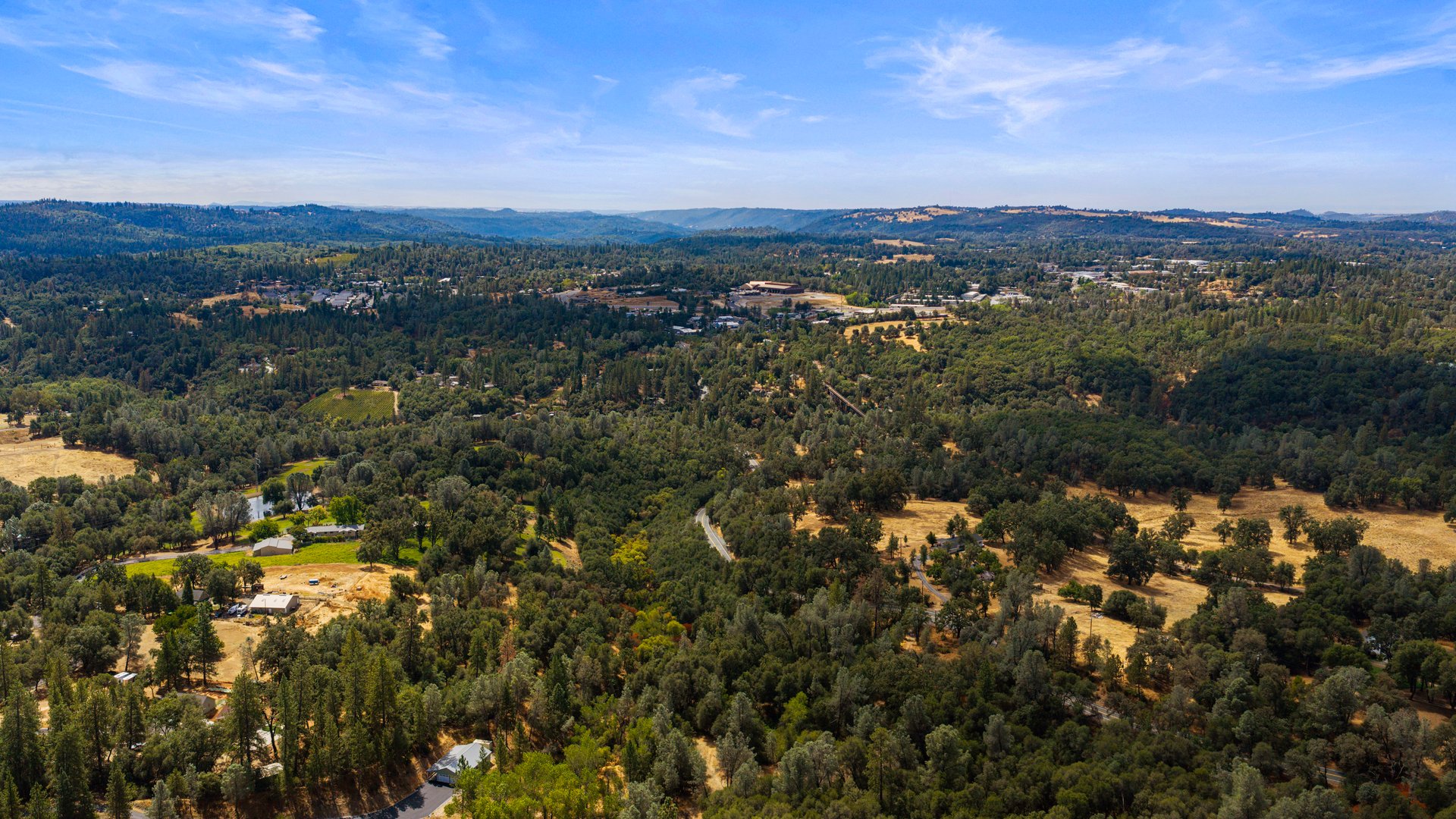 Aerial view of wooded rural land with scattered homes, fields, and rolling hills.